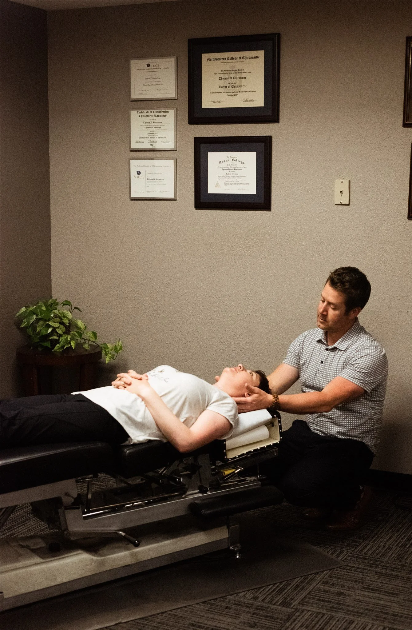 Chiropractor performing neck adjustments on a patient lying face up on an adjustment table in a chiropractic office.