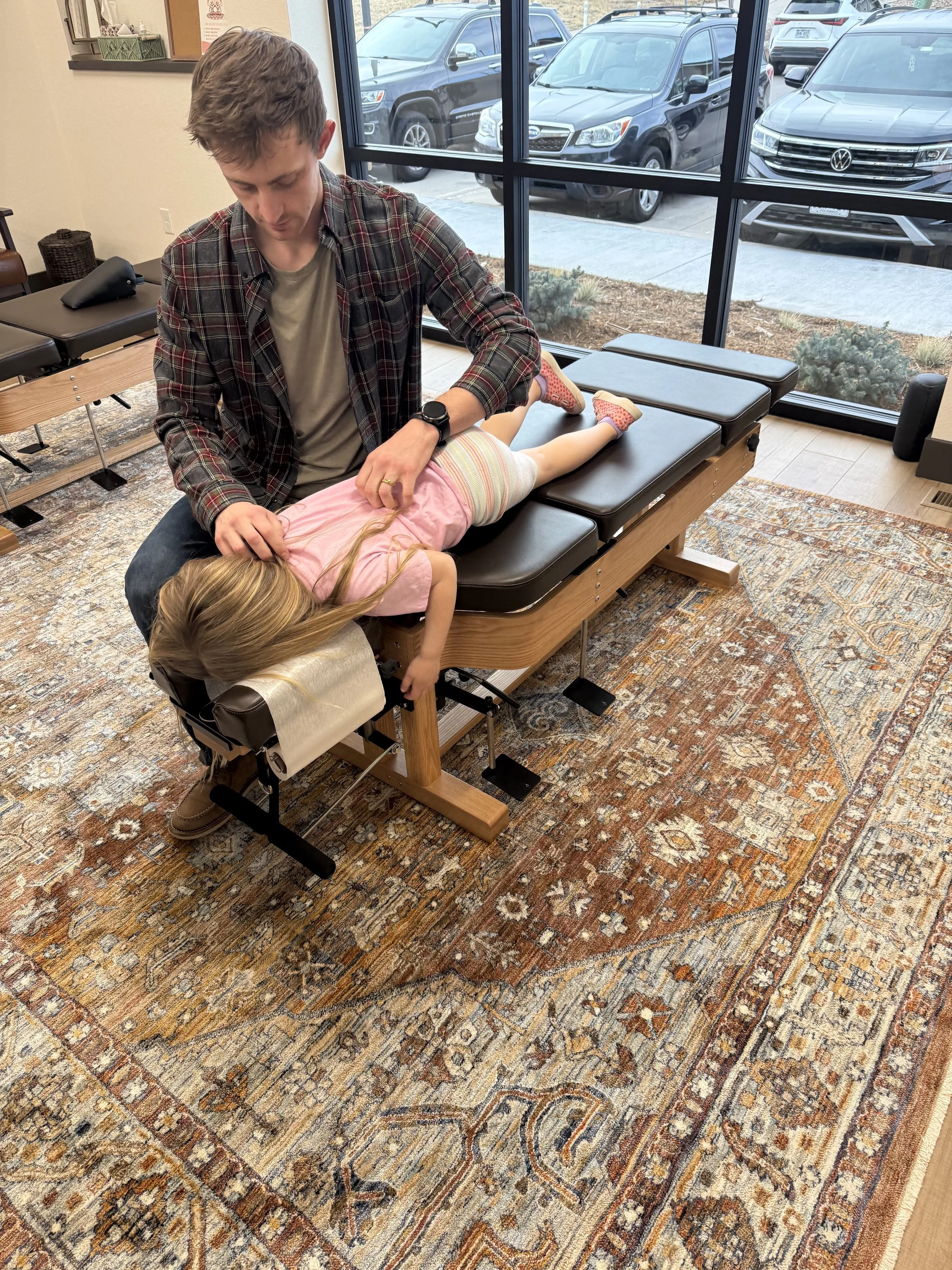 A woman smiling next to a young boy sitting in a wheelchair with a head and neck support, in a healthcare setting.