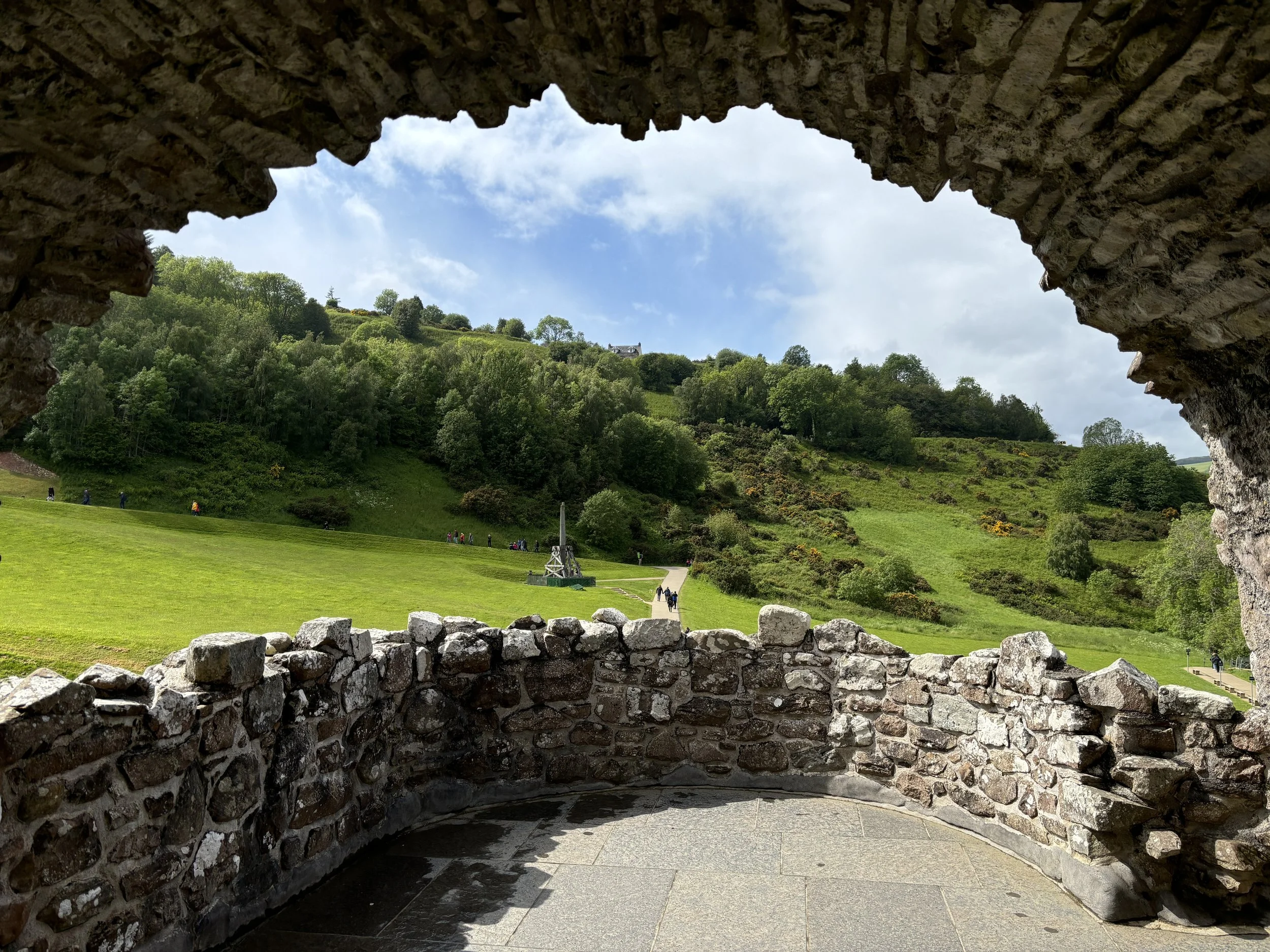 Scenic view of green hillside through a stone window frame with cloudy sky