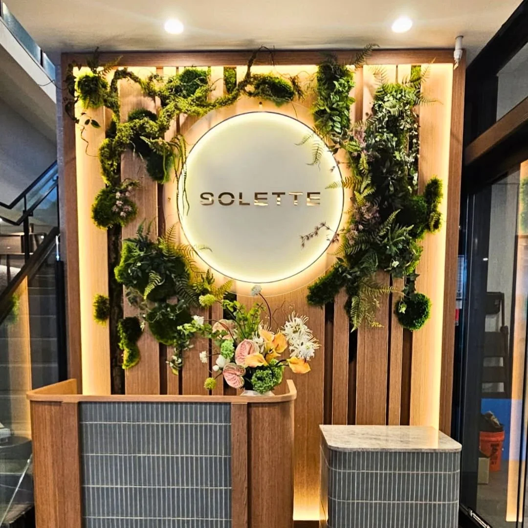 Dense green wall with various types of moss, succulents, and small plants, some with white and yellow decorative elements.