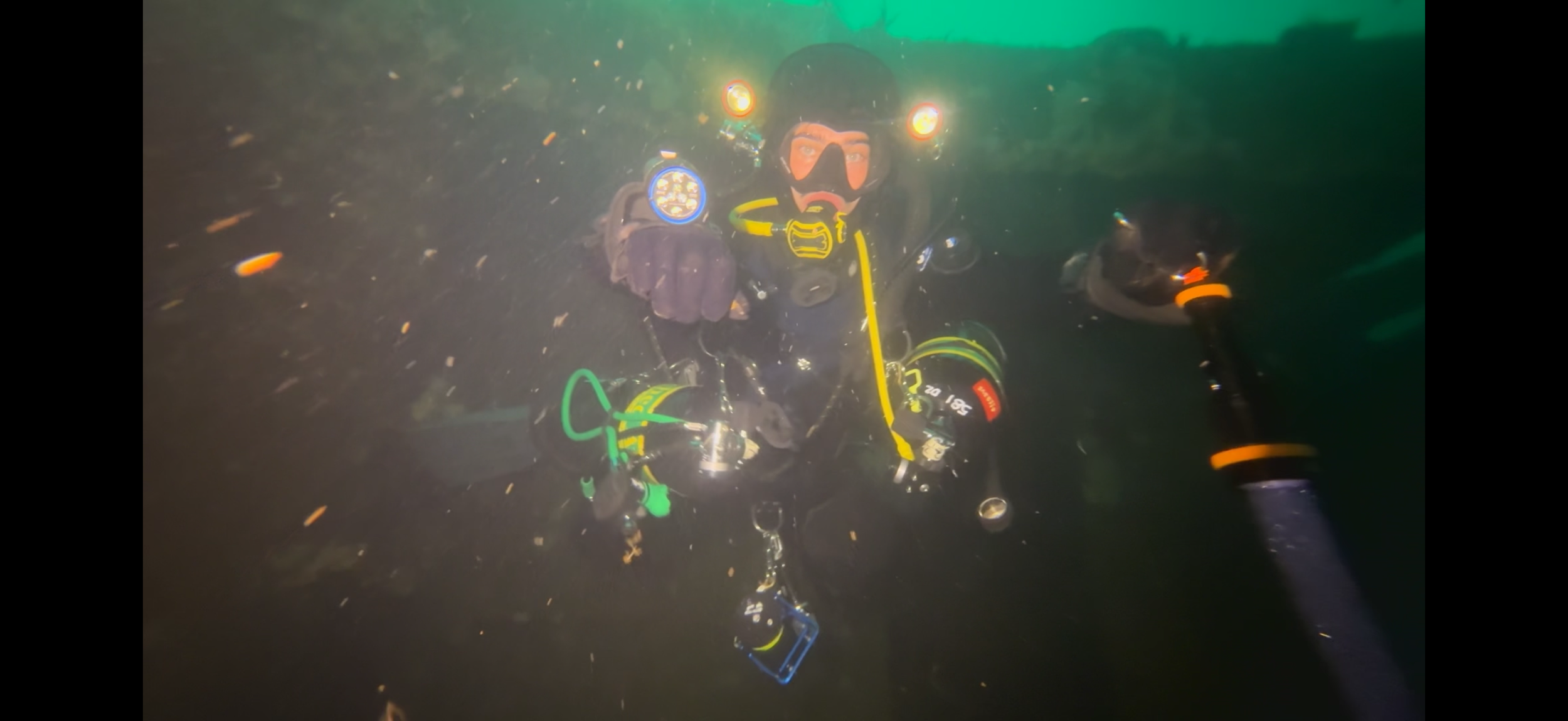 A diver wearing a black helmet and full firefighting gear, including a mask and oxygen tank, standing outdoors during nighttime