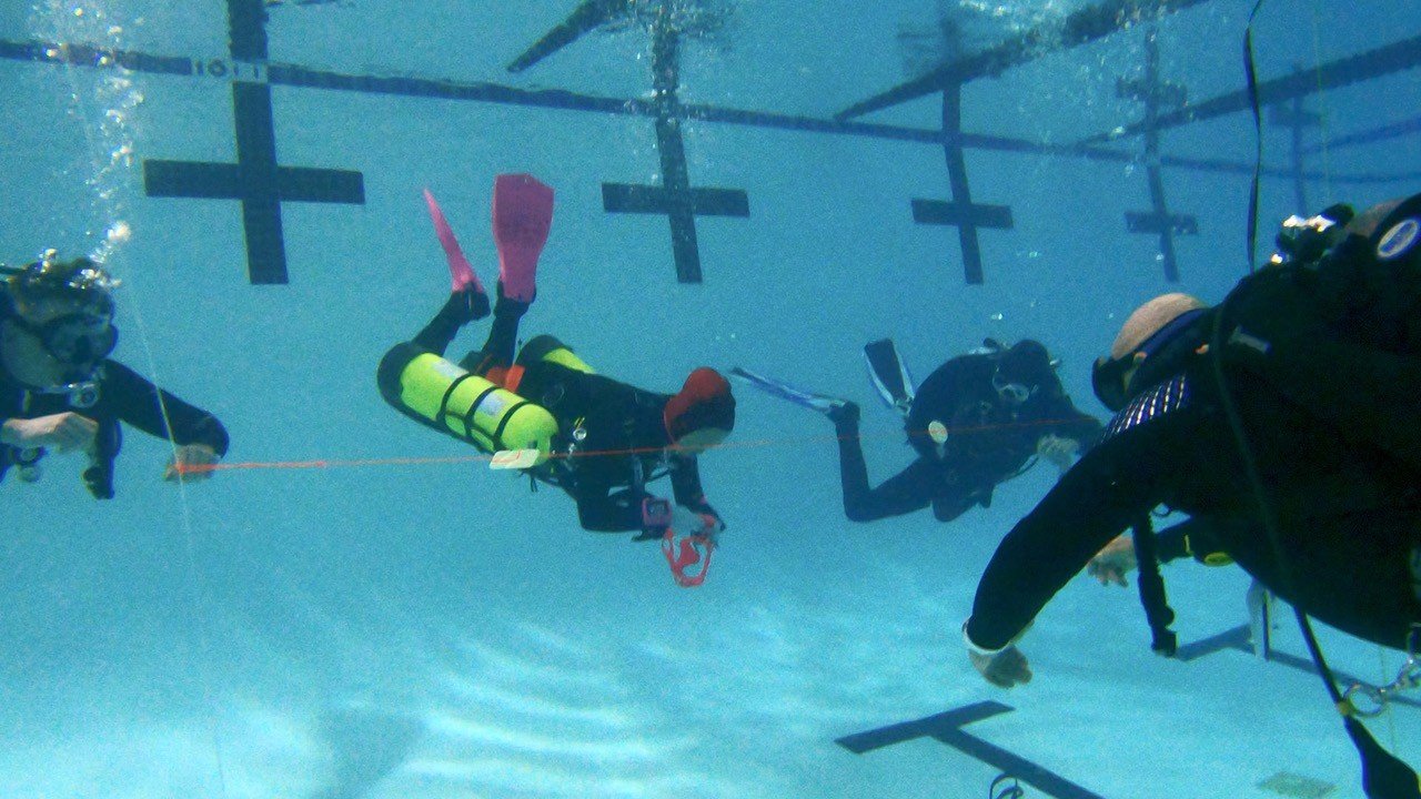 Three scuba divers underwater practicing rescue skills next to a buoy line and scuba training platforms.