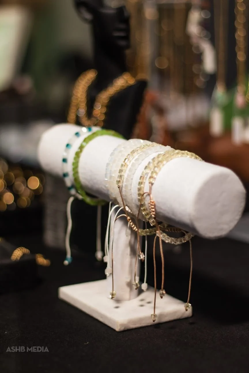 A jewelry display stand with various bracelets and bangles, including gold, silver, and beaded designs, on a white cylindrical holder at a jewelry shop.
