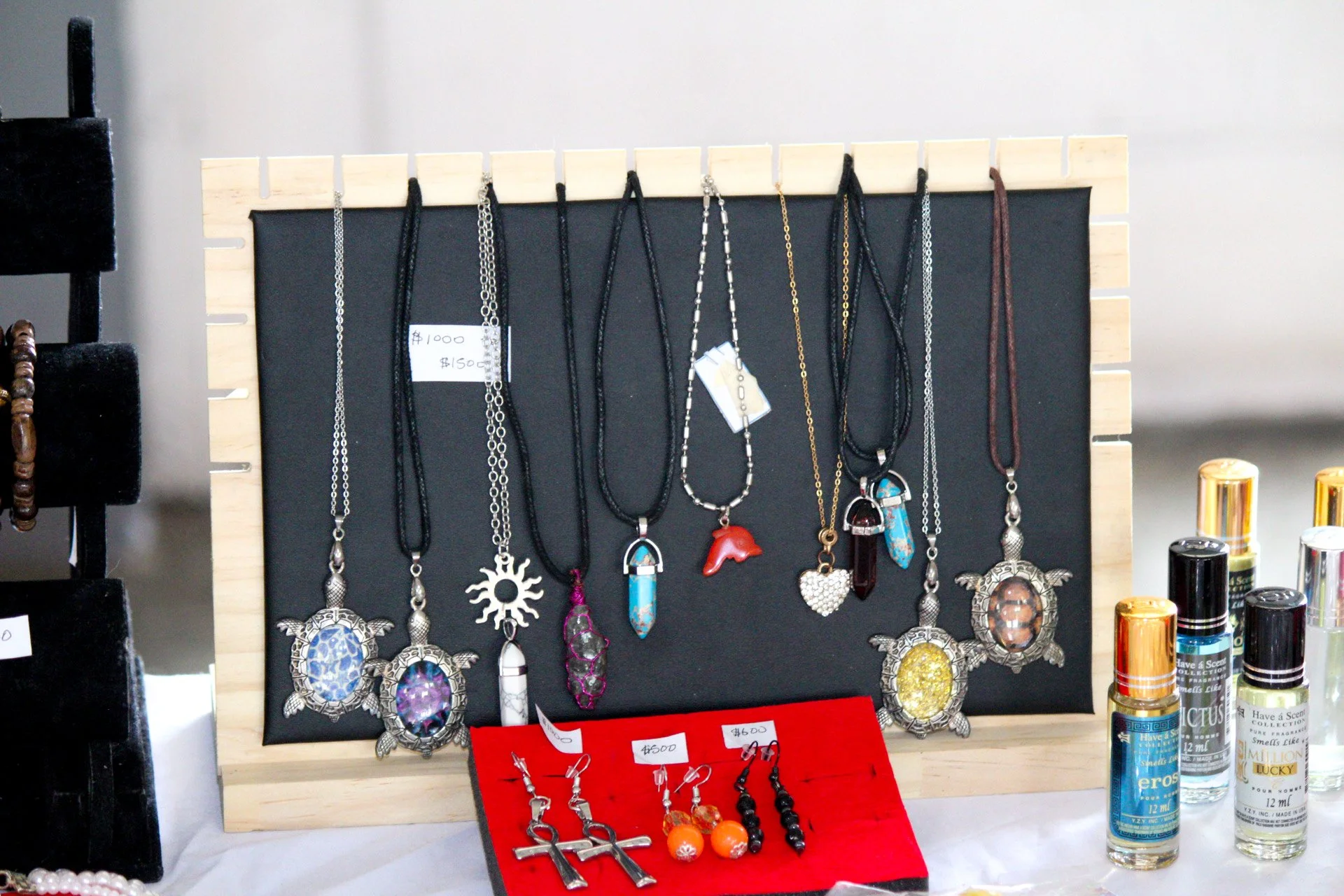 Display of necklaces and earrings on a black board and red stand, with perfume bottles on the side.