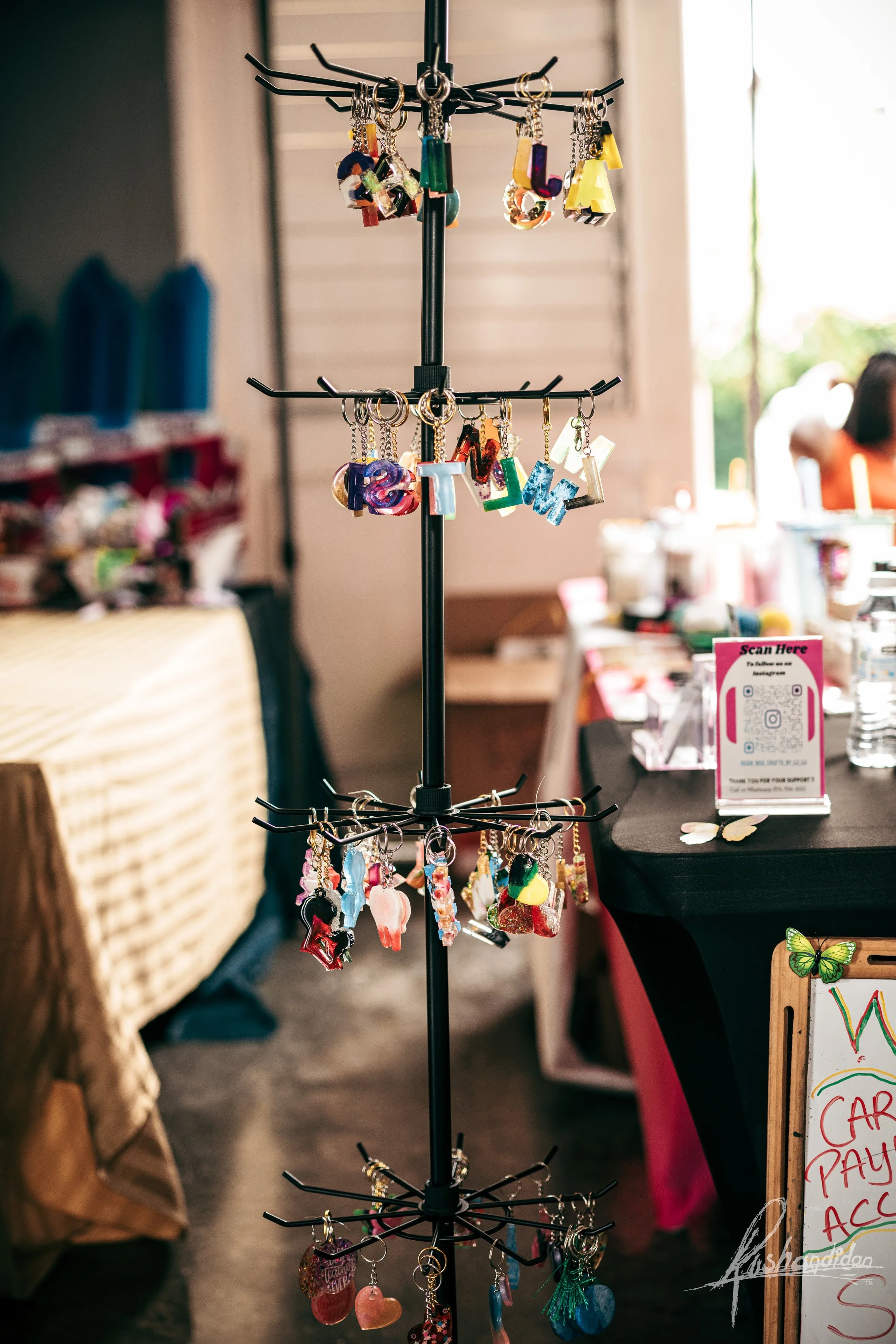 A jewelry display stand with colorful keychains and charms hanging on multiple tiers at an indoor market or craft fair.