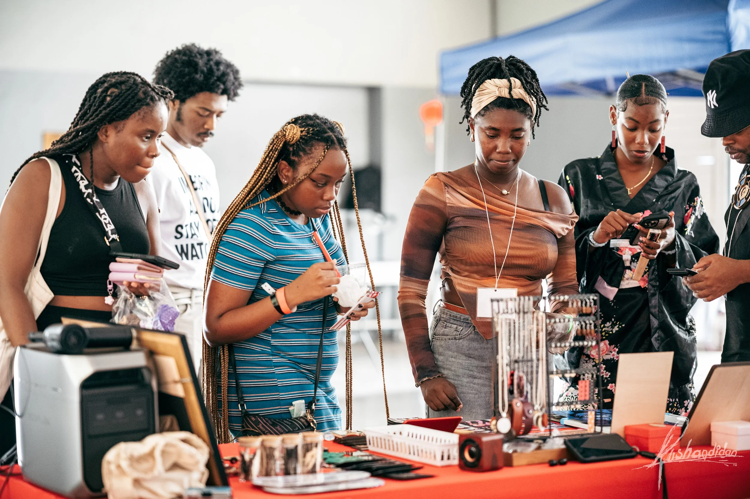 Group of six people shopping at a market stall with jewelry, listening to music, and taking photos.