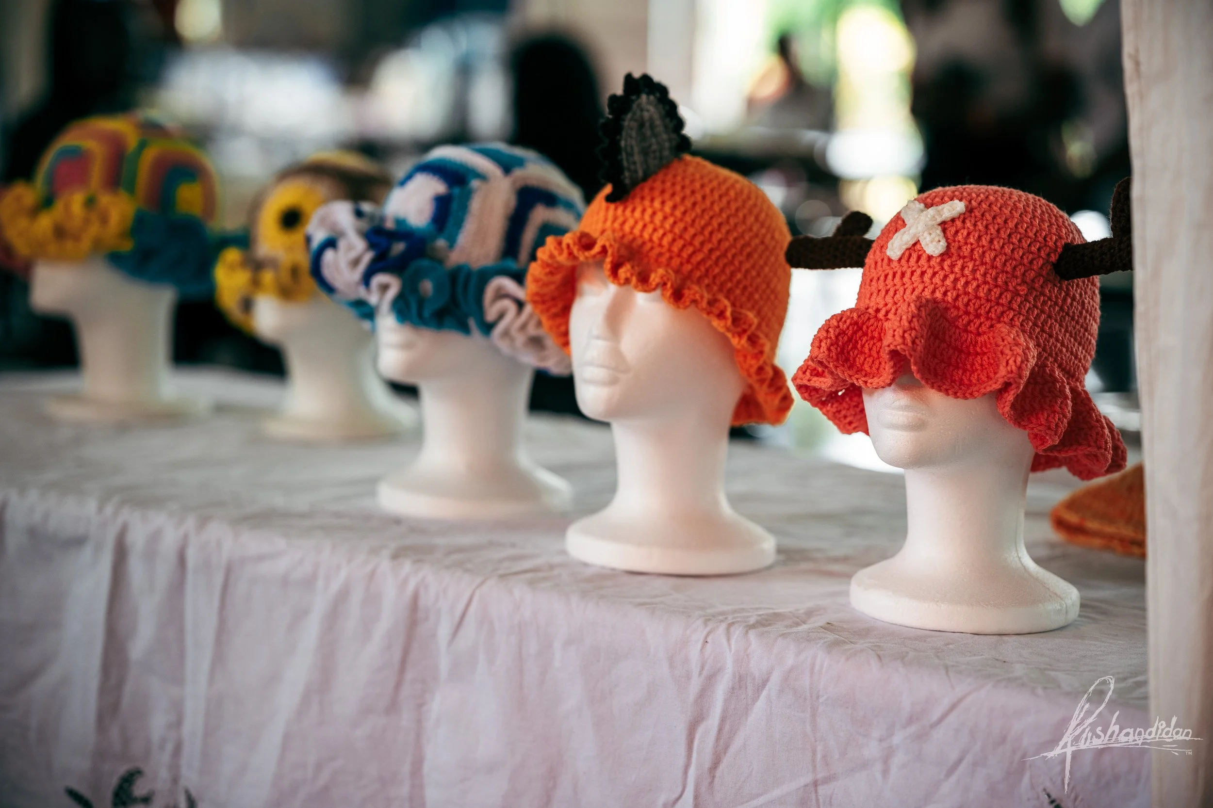 Display of colorful crochet hats on mannequin heads at a market stall.