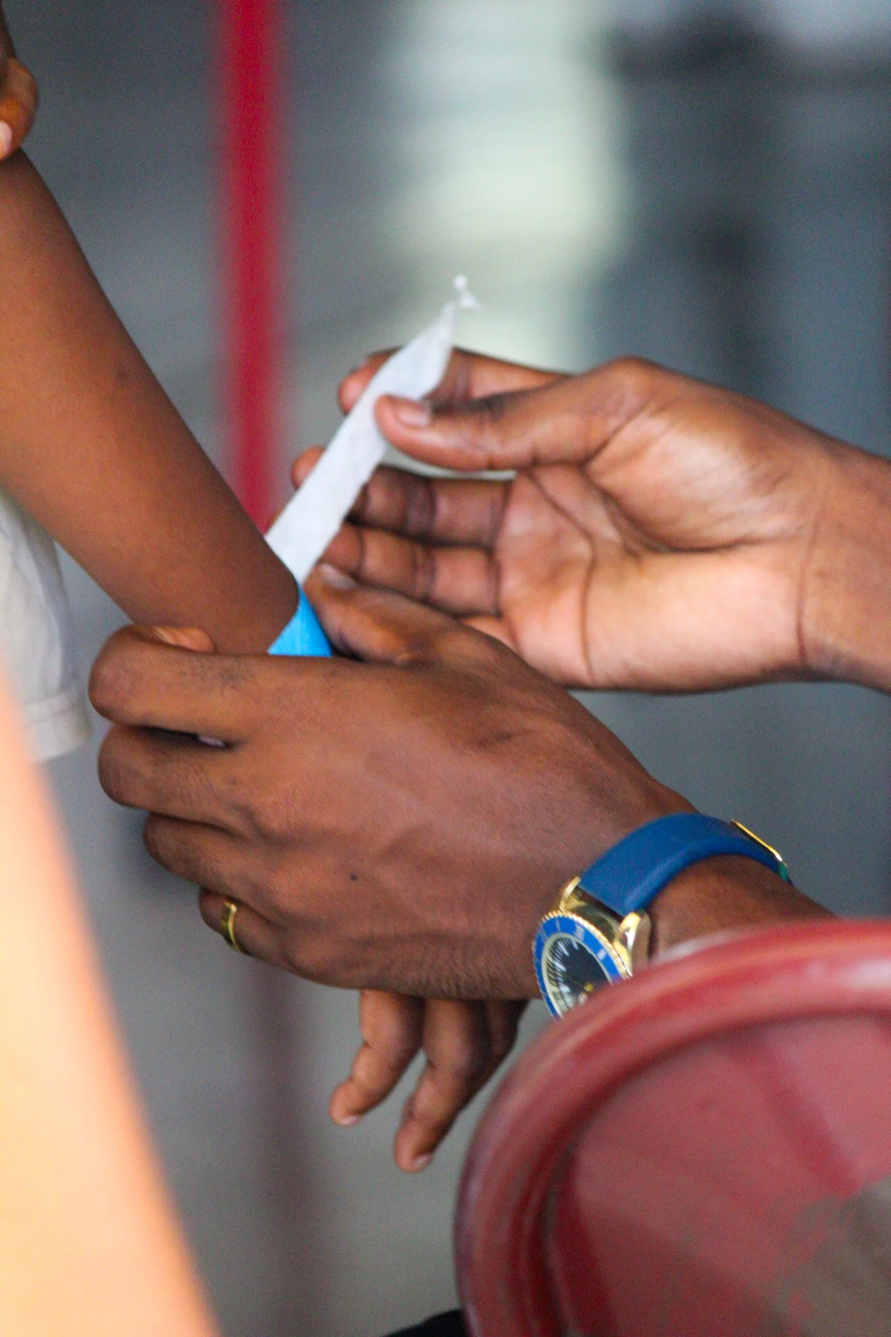 A person with a blue wristwatch helping another person with a bandage.
