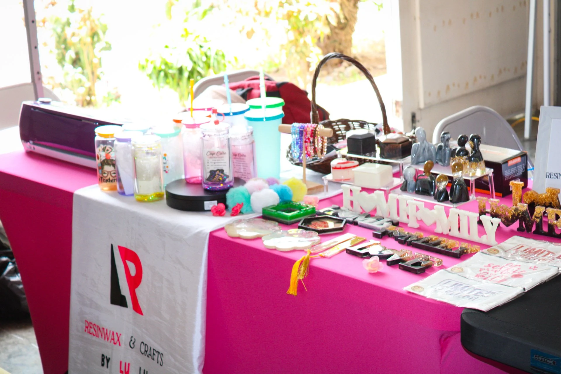 Display table with resin crafts items and decorations at a craft fair, including colorful resin figurines, letters, and jars with epoxy resin.