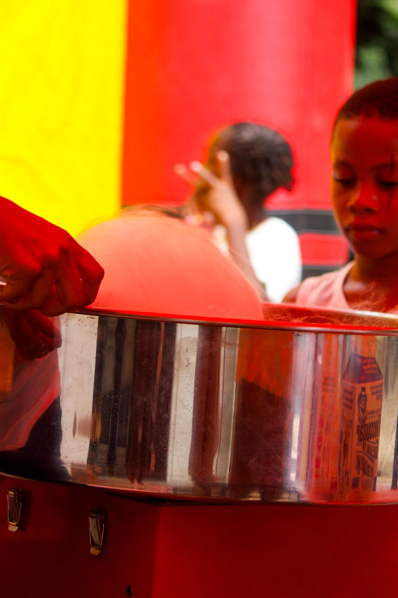 Children playing at a cotton candy stand with red and yellow background.