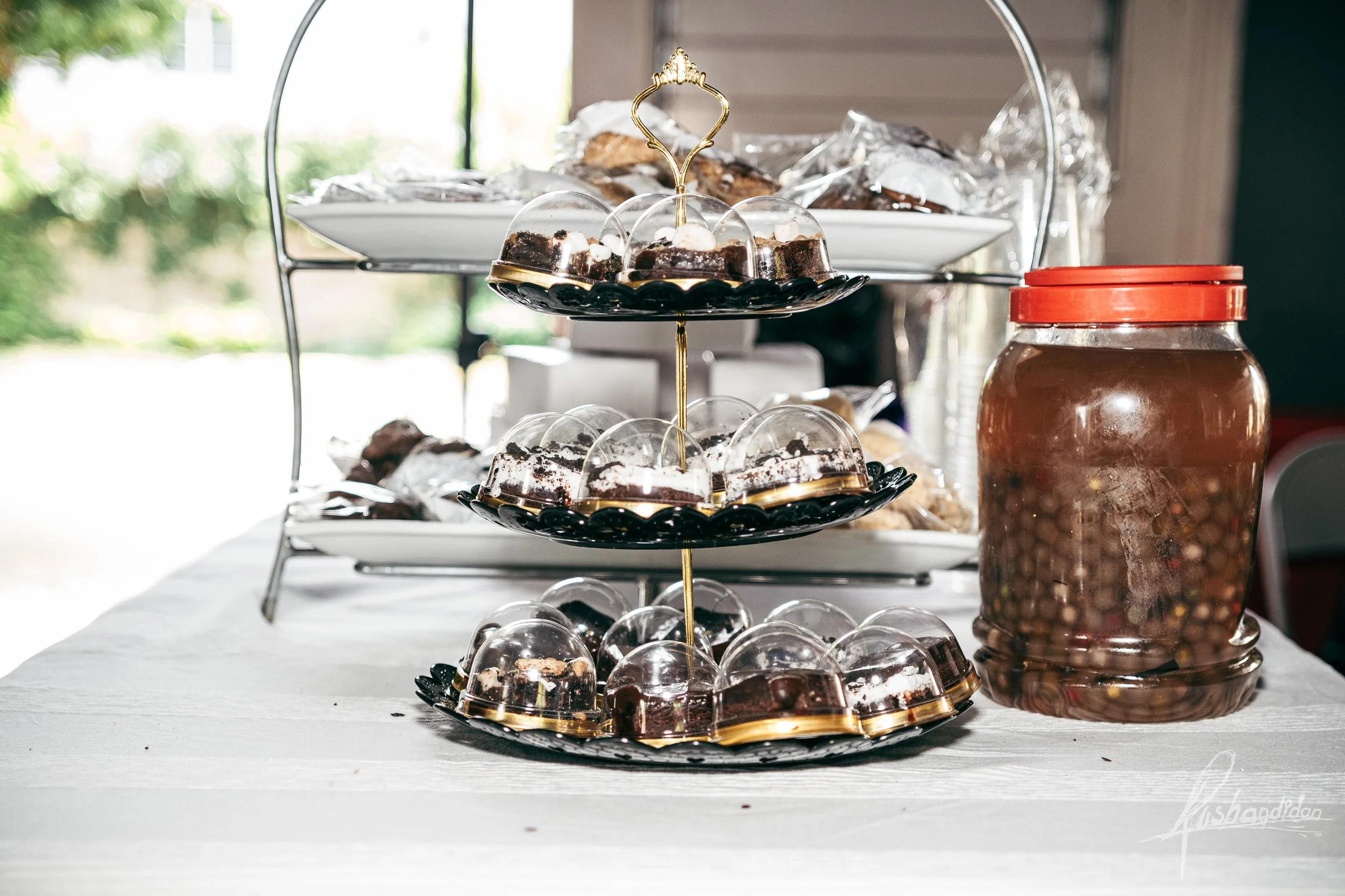 Three-tiered serving stand with assorted chocolate and dessert treats and a jar of chocolate candies on a white table.