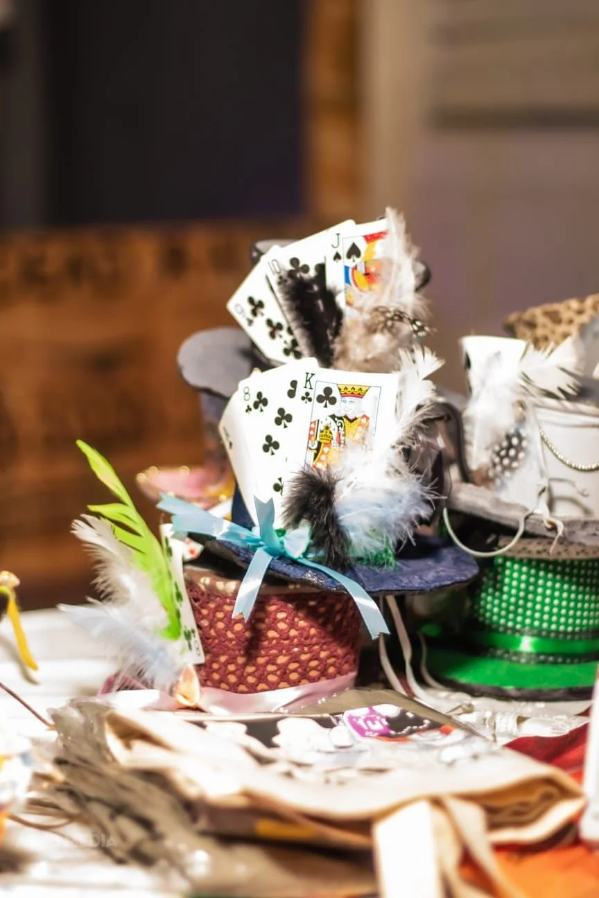 Deck of playing cards decorated with colorful feathers and tied with ribbons, displayed on a table with other decorative items.