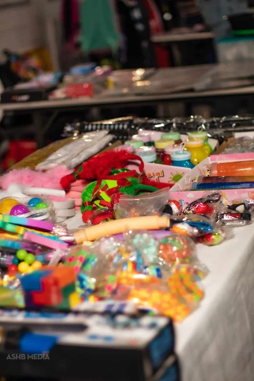 Display of colorful small toys, hair accessories, and decorative items spread across a table at a market or store.