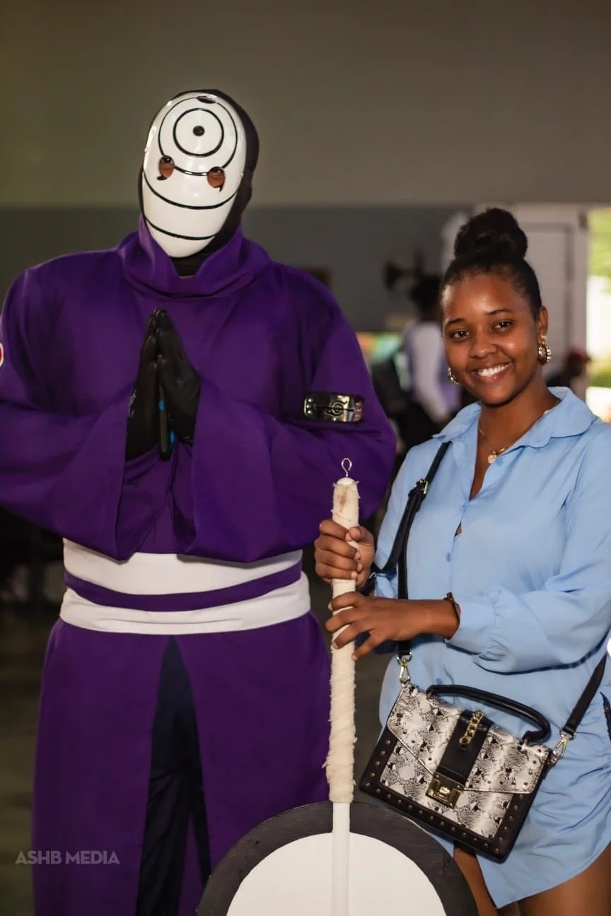 A woman with a dark bun hairstyle wearing a light blue dress holding a large white candle, standing next to someone in a purple costume with a white mask featuring a target or bullseye design, some small brown spots, and hands in a prayer position, i