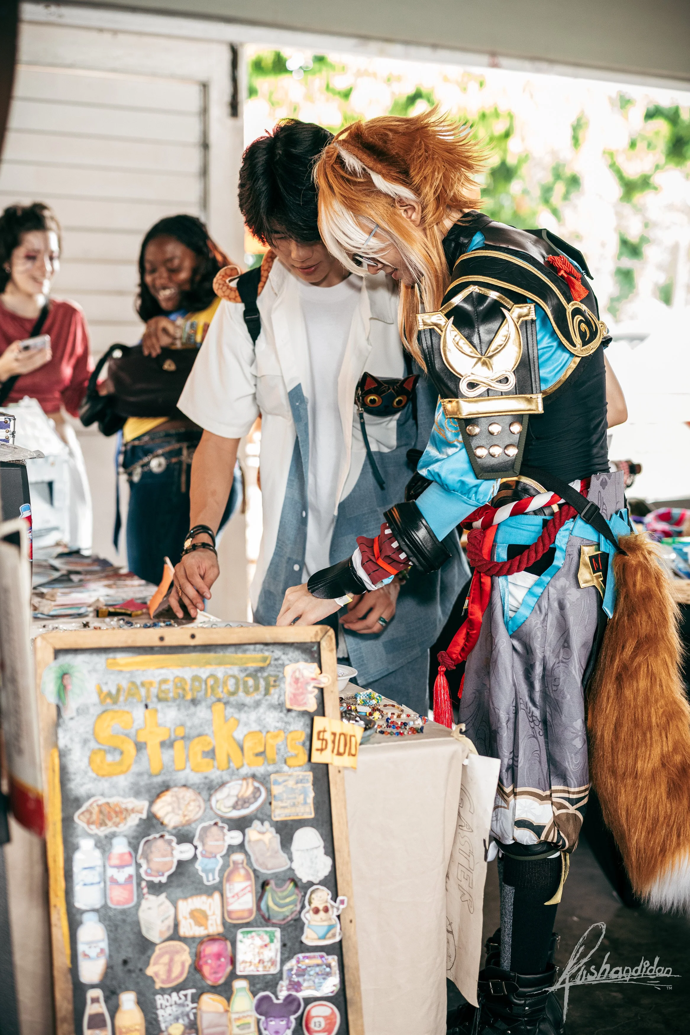 People shopping at a marketplace stall with a sign selling waterproof stickers for $1.00.