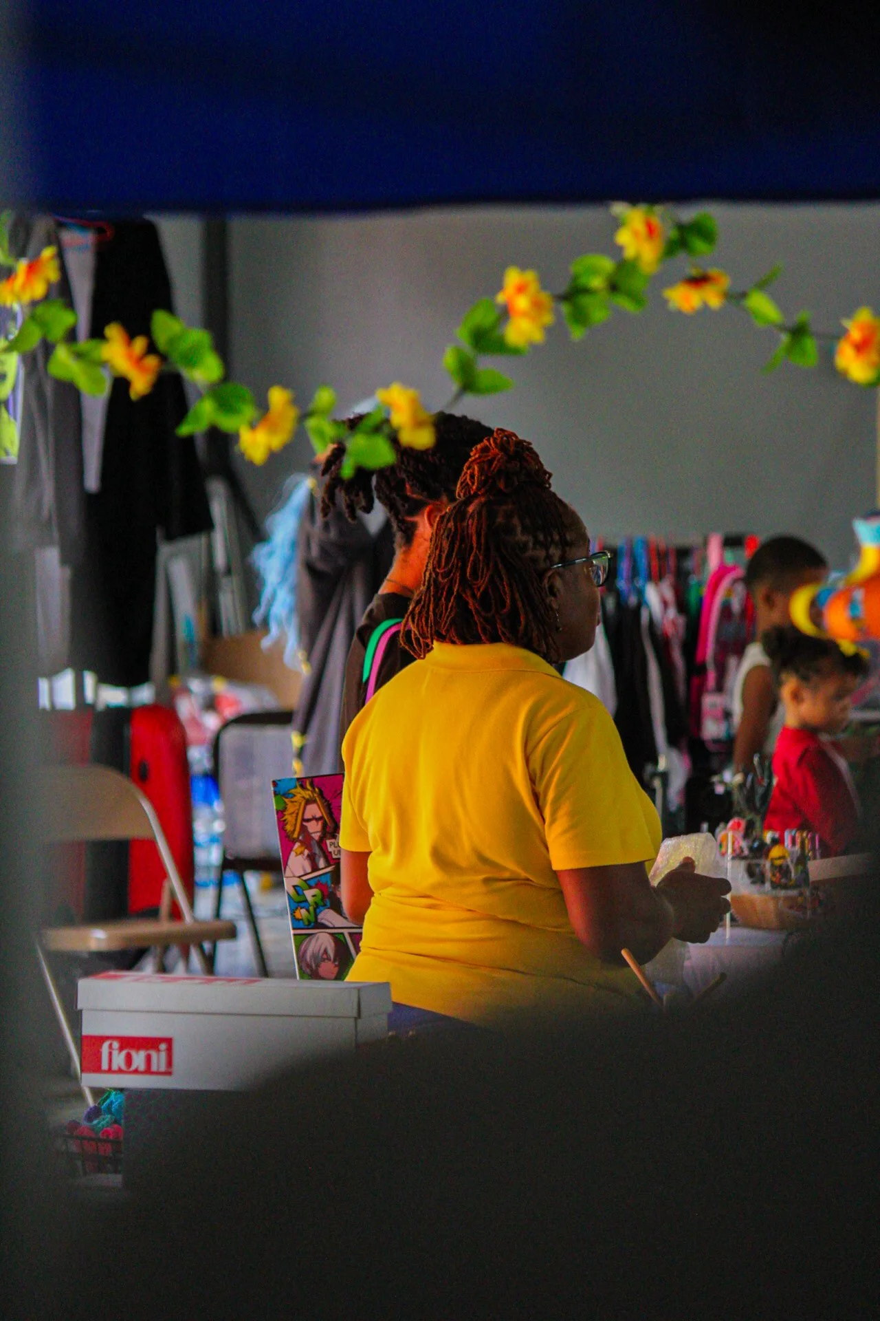 People at a table with toys on display, surrounded by hanging children's backpacks and colorful decorations.