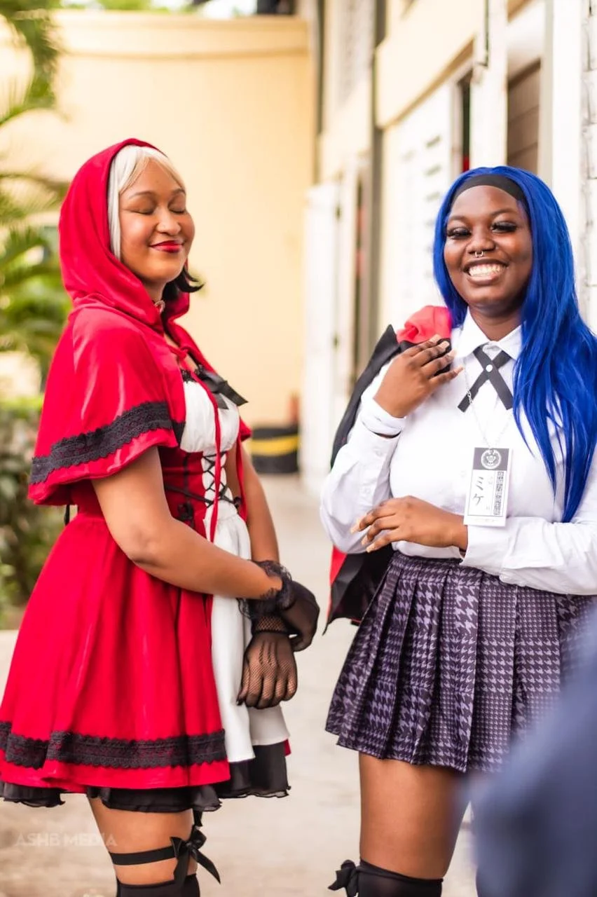 Two women dressed in cosplay costumes standing outdoors, smiling and looking happy.