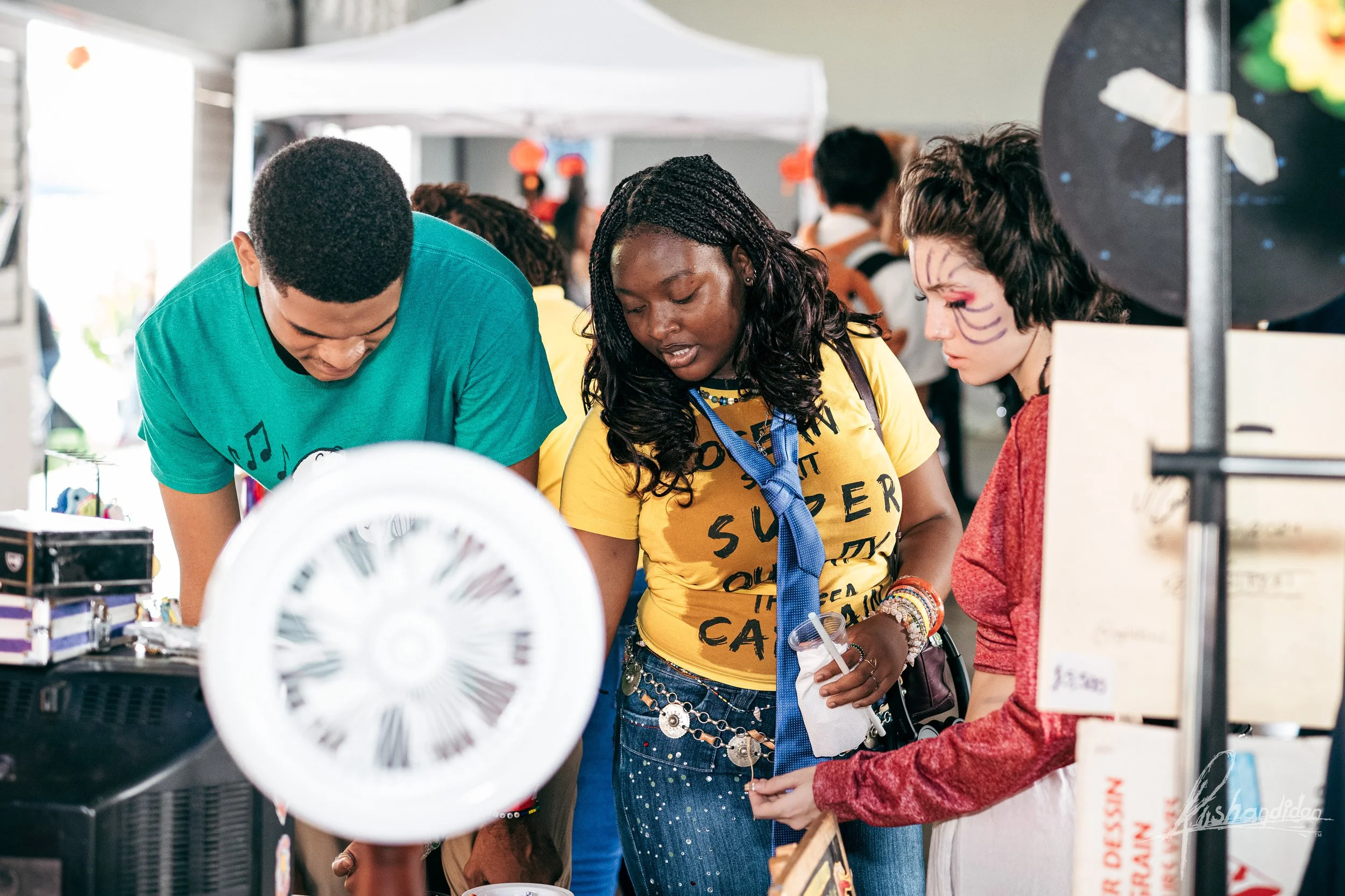 A group of people at a booth, looking at items on display, with one person dressed with Halloween makeup.
