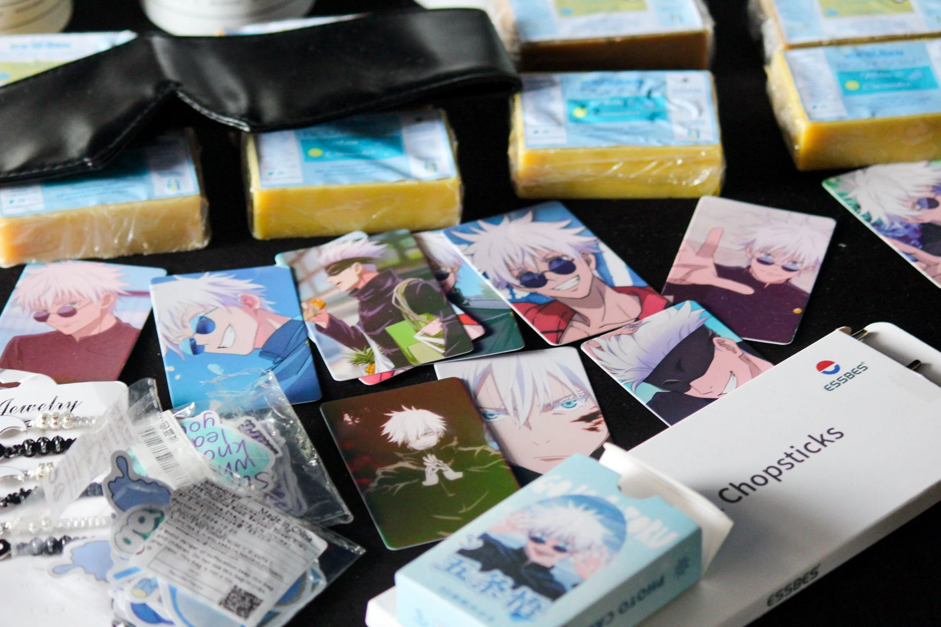 Collection of anime-style character cards, soap bars, jewelry, and chopsticks on a black surface.