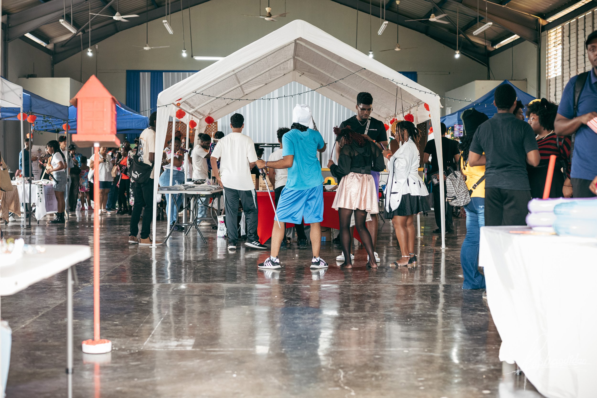 People browsing booths at an indoor market or fair with tents and tables set up inside a spacious hall.