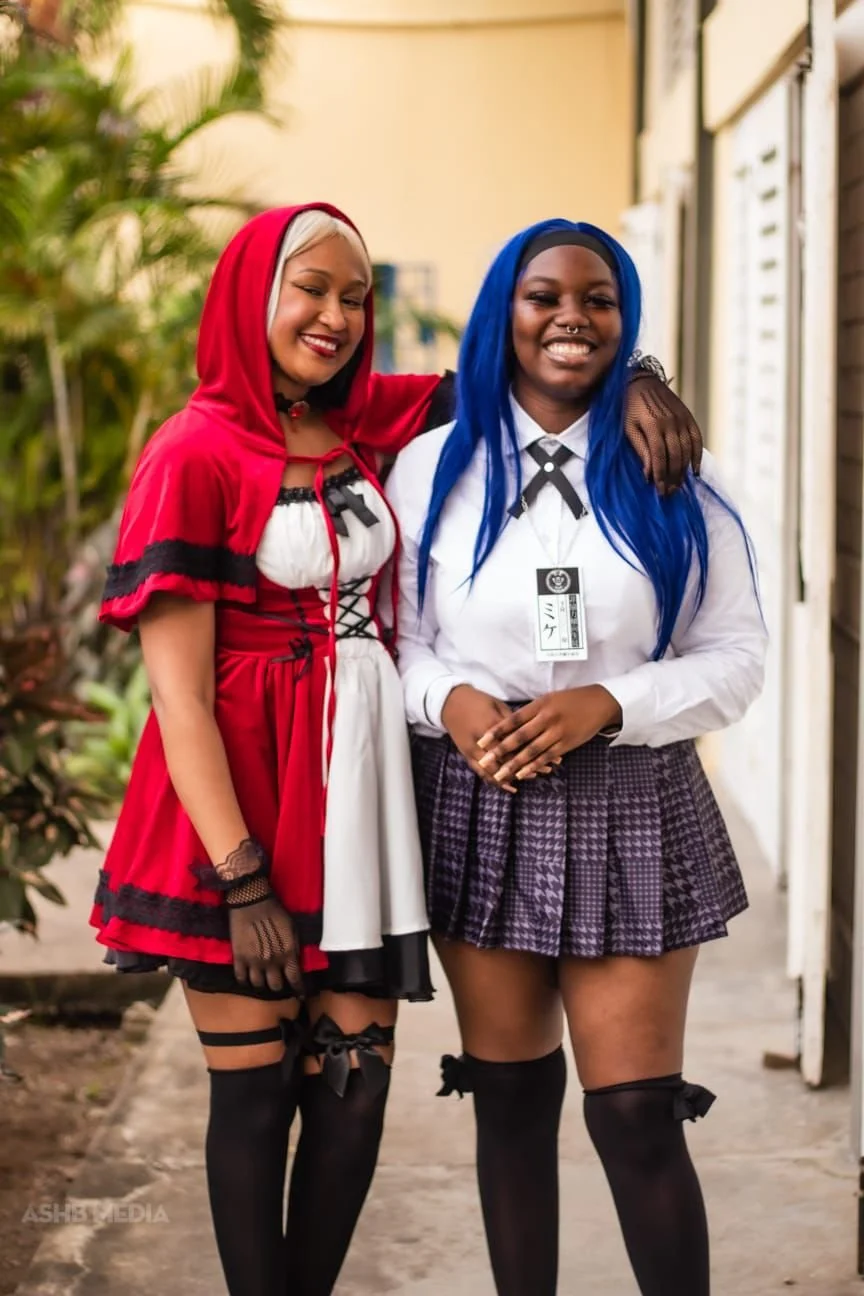 Two women dressed in cosplay costumes standing outside, smiling and posing for a photo with their arms around each other.