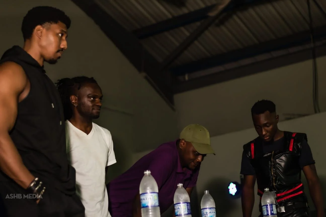 Four men standing around a table with water bottles, inside a room with a high ceiling.