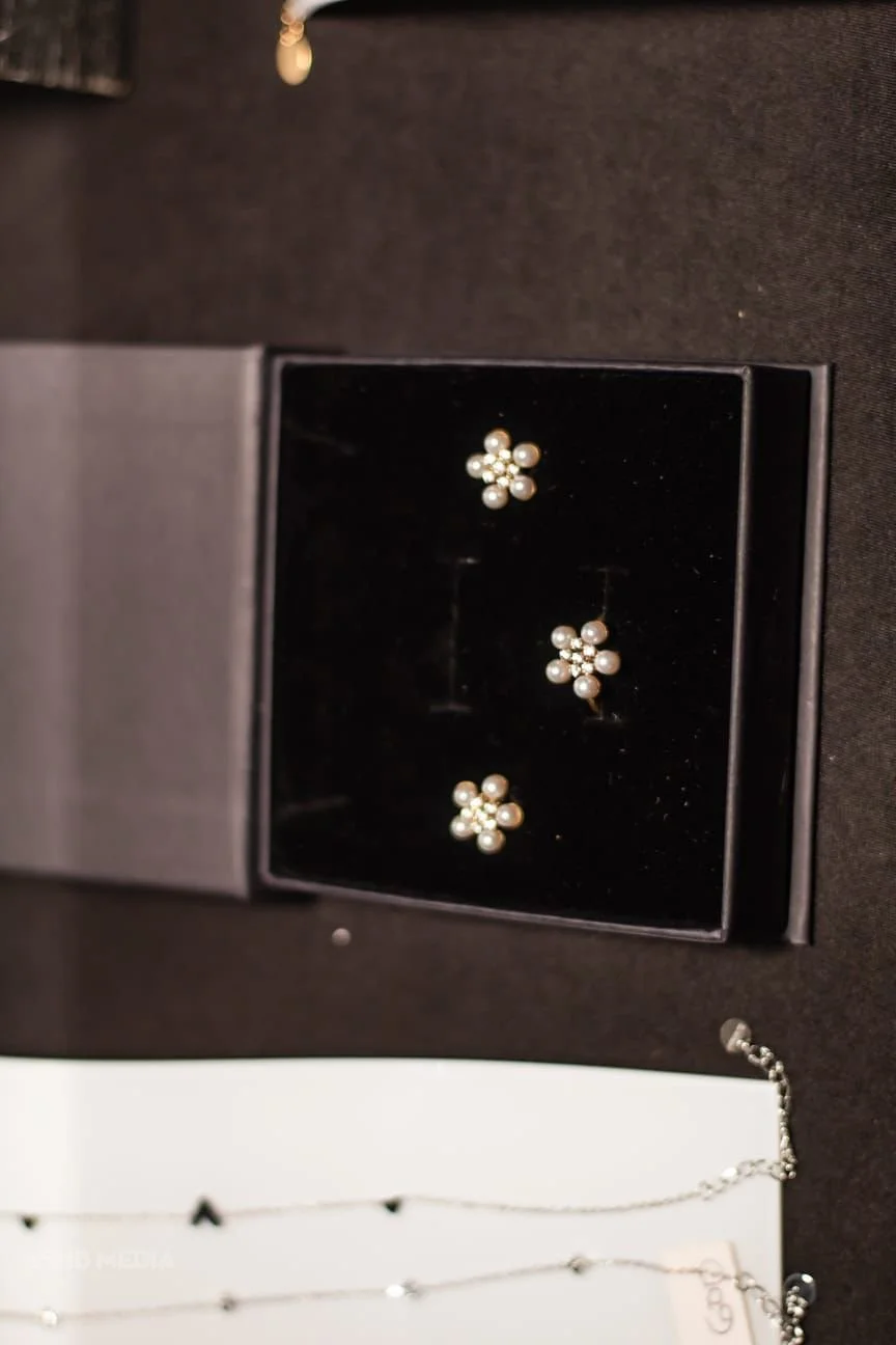 A pair of pearl and rhinestone flower-shaped earrings and a matching necklace in a black jewelry box on a dark surface.
