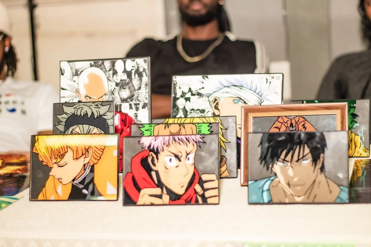 Collection of framed anime character illustrations displayed on a table at a convention.
