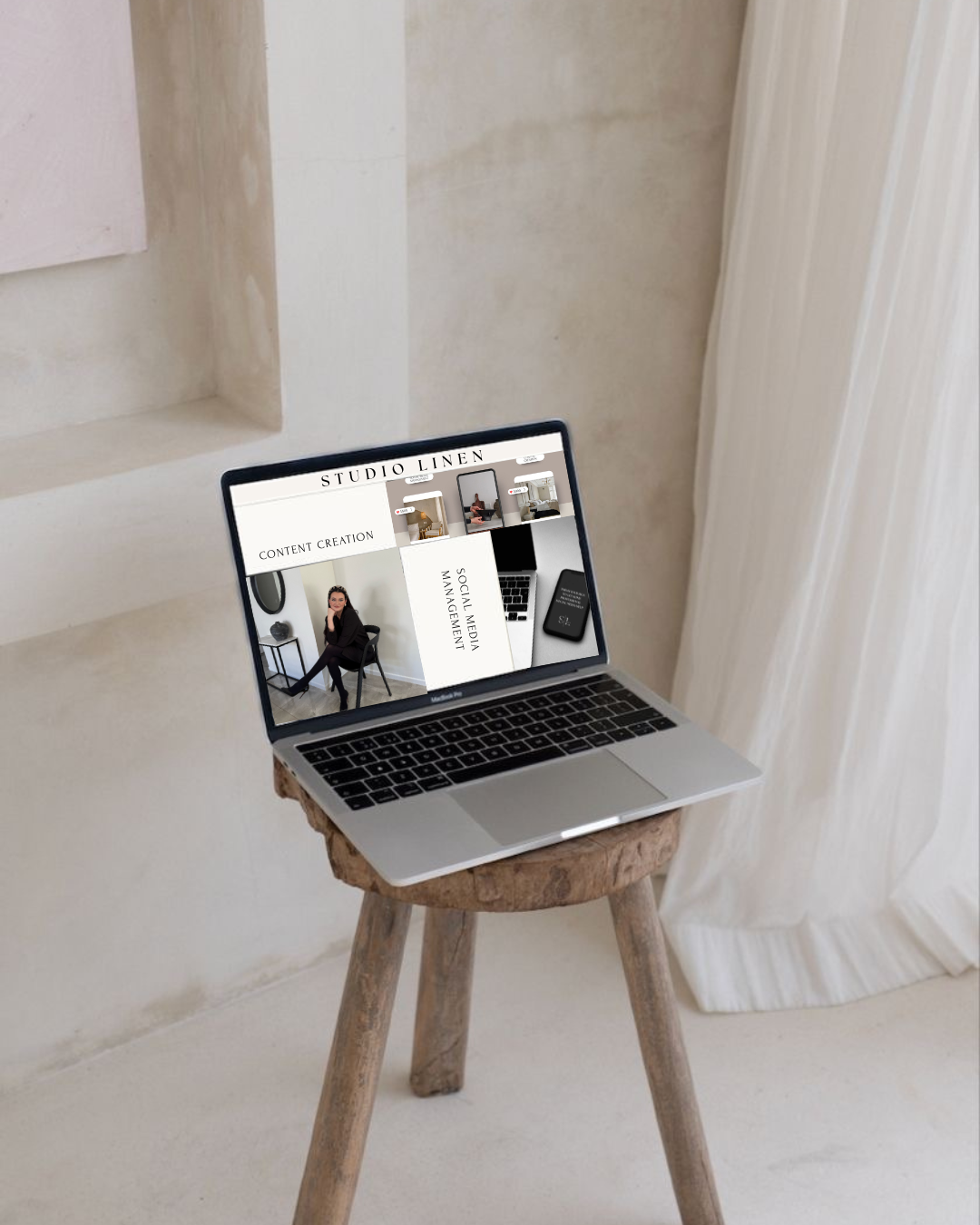 A laptop on a wooden stool displaying a website with the title 'Studio Linen' and sections for content creation and social media management, in a minimalistic room with white walls and curtains.