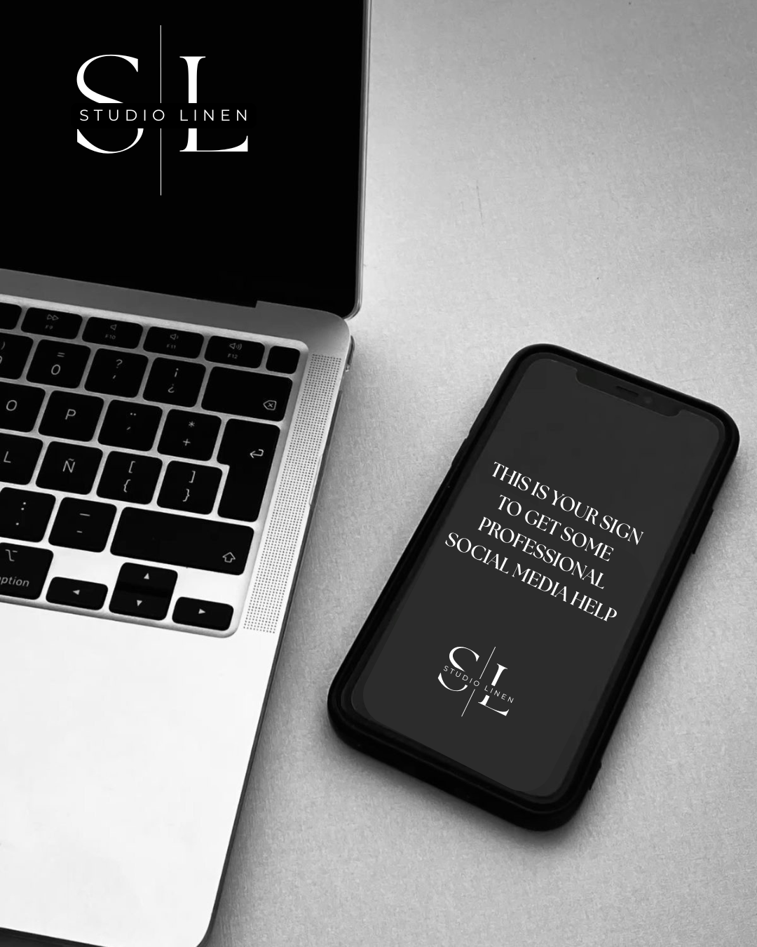 Black and white photo of a MacBook laptop and an iPhone on a light-colored surface. The MacBook shows part of its keyboard, and the iPhone screen displays text saying, "This is your sign to get some professional social media help," along with the Studio Linen logo.