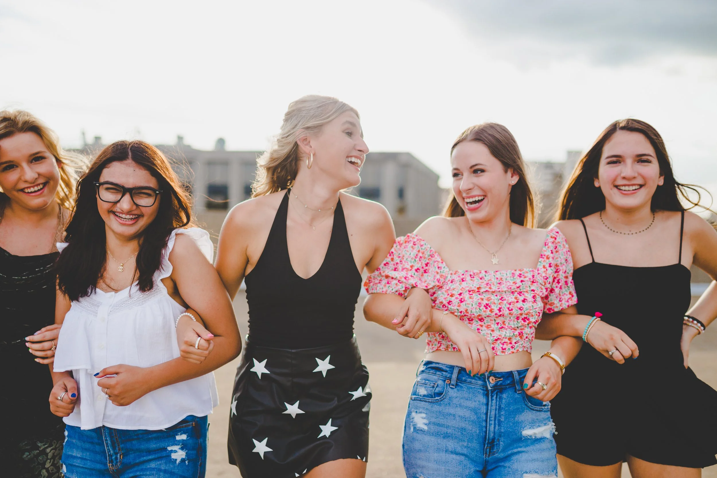 Five young women are walking outdoors, smiling, and enjoying each other's company.