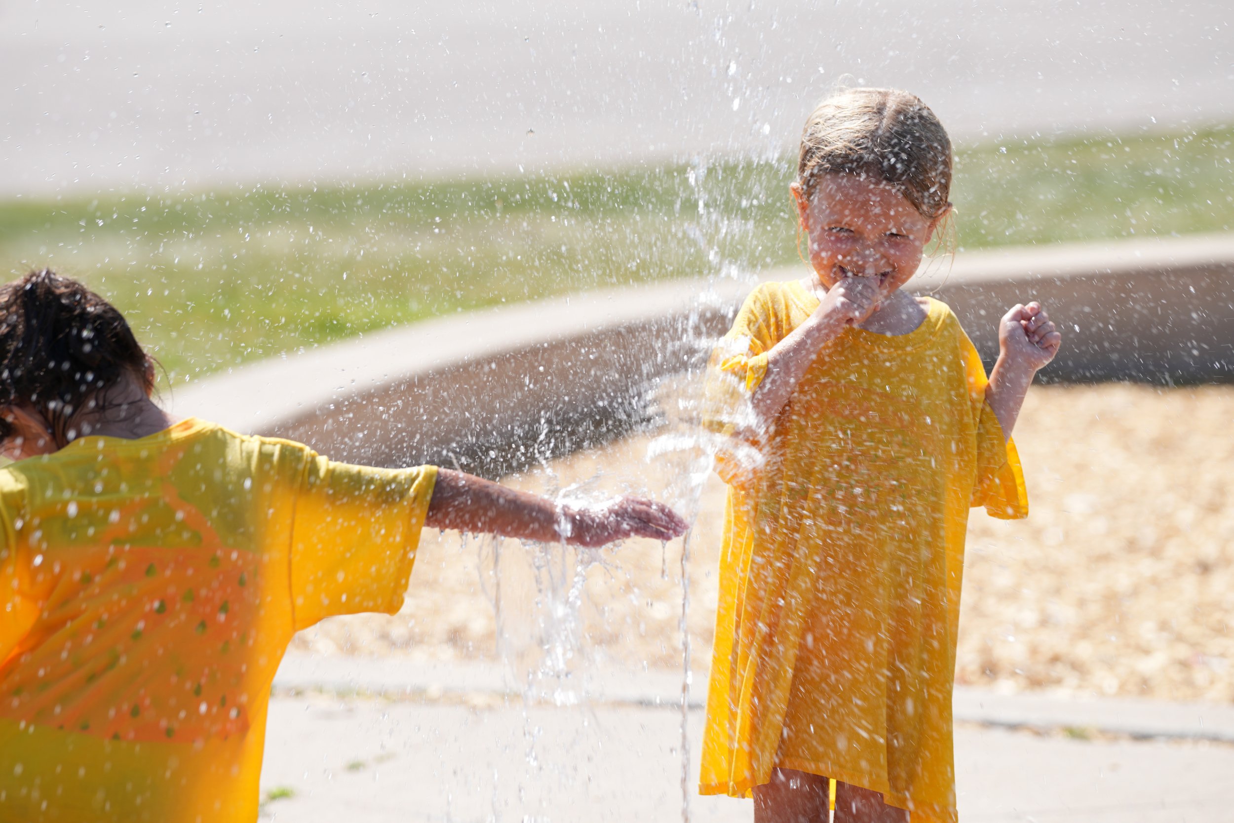 Two children playing in the water, wearing yellow shirts, and smiling as they splash water on each other.