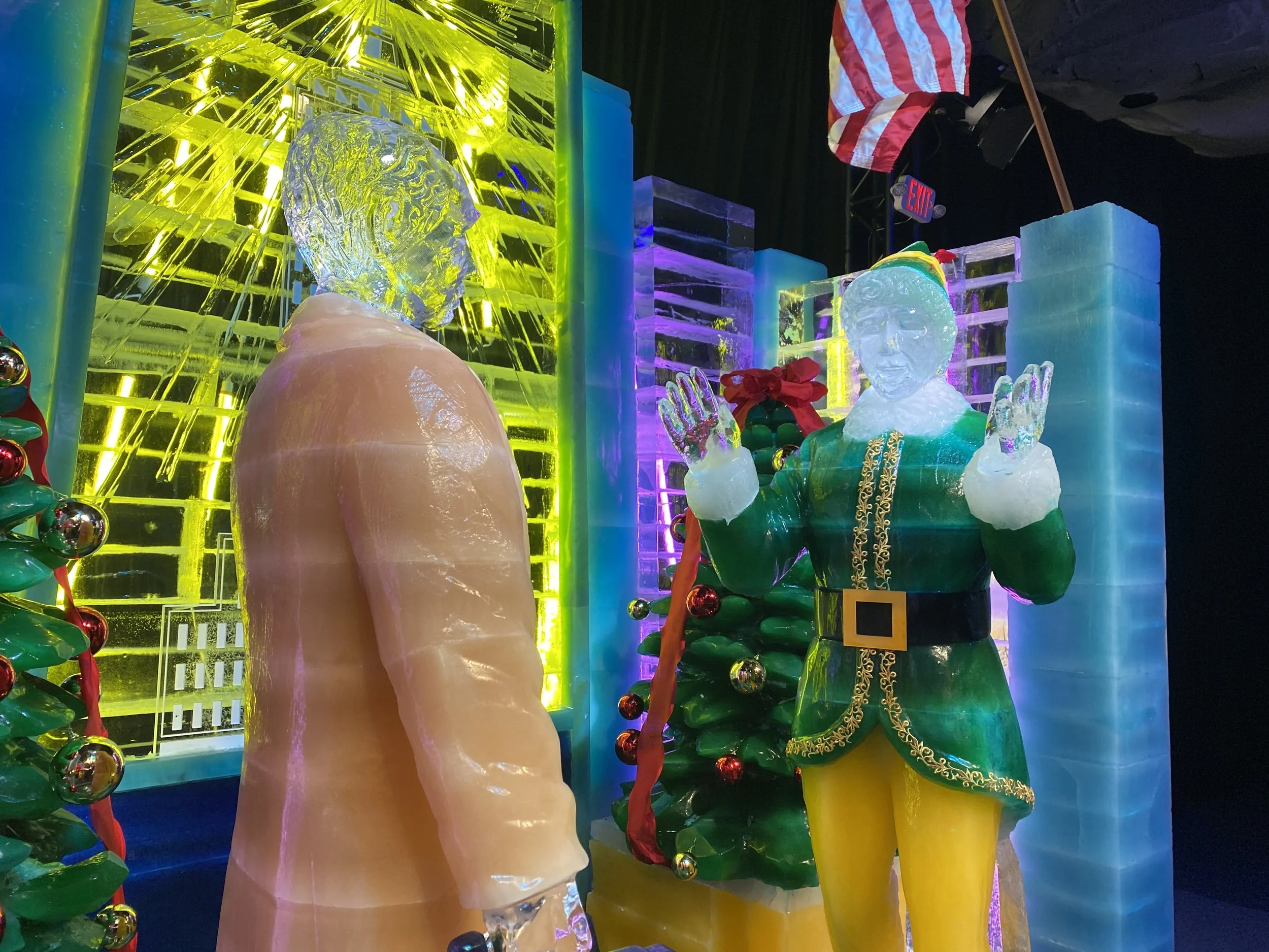Ice sculptures of a human face, a woman with clasped hands, and a Christmas tree with ornaments, all illuminated by colorful lights.