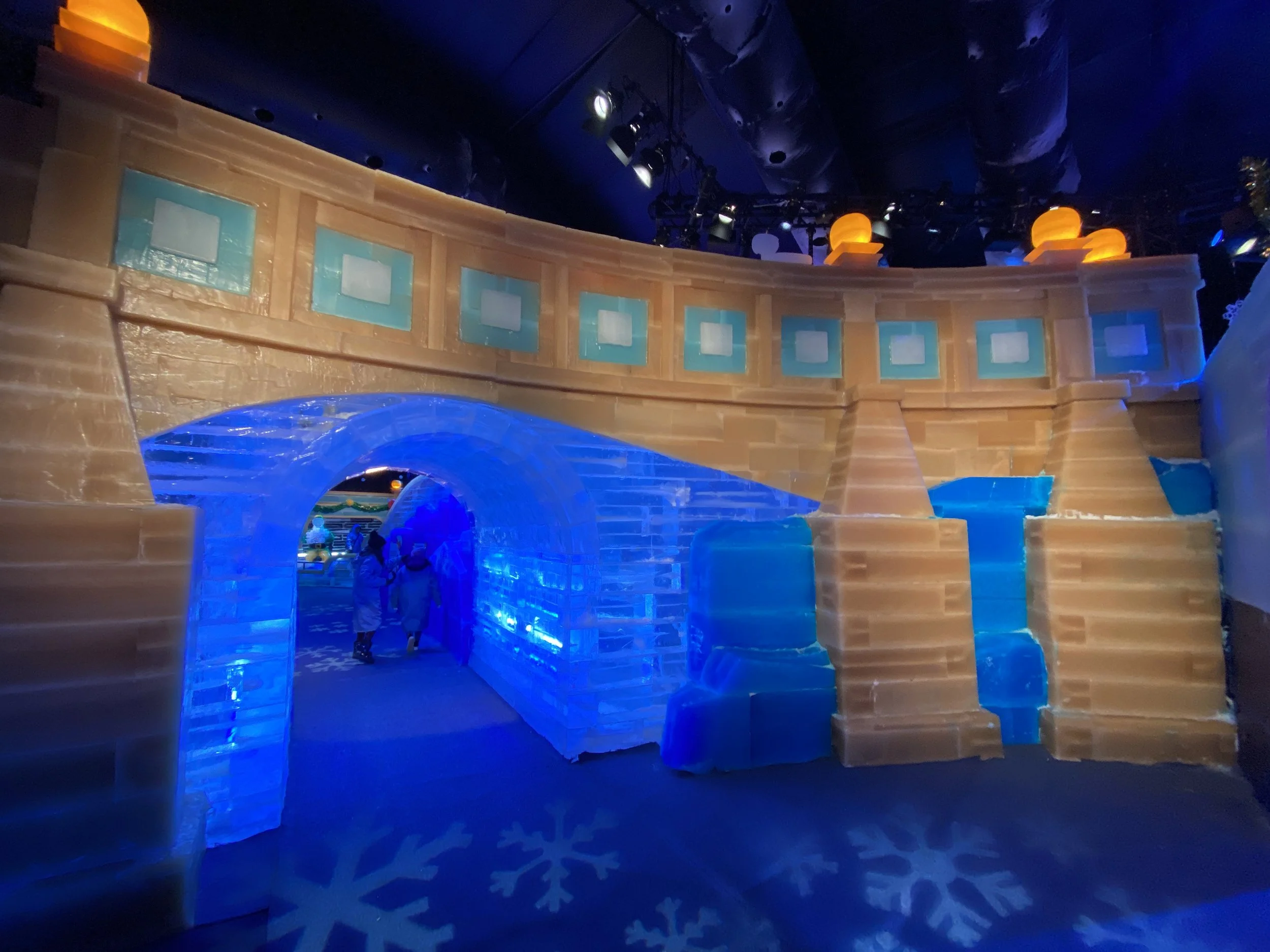 Ice castle with blue lighting, featuring arches and windows, and glowing orange lights on top.