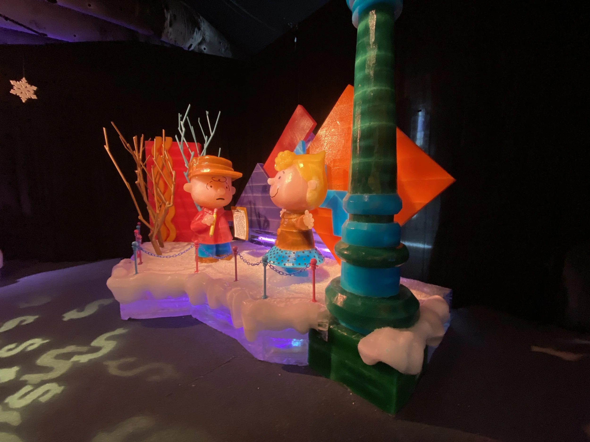 Colorful illuminated sculptures resembling characters and objects in a dark room with projected patterns on the floor.