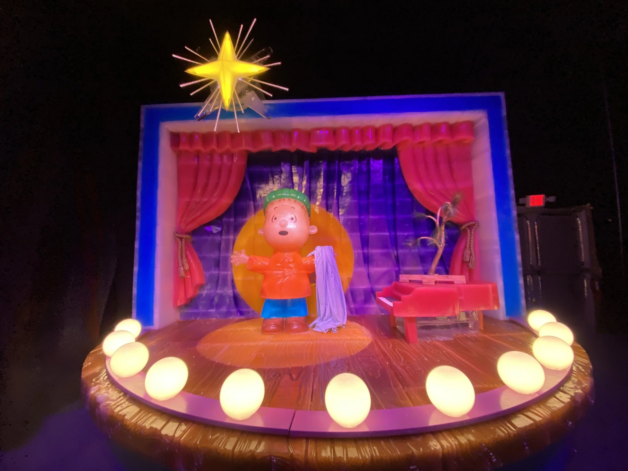 Colorful display with a cartoon character in front of a stage with red curtains and a yellow star on top, surrounded by yellow glowing orbs.