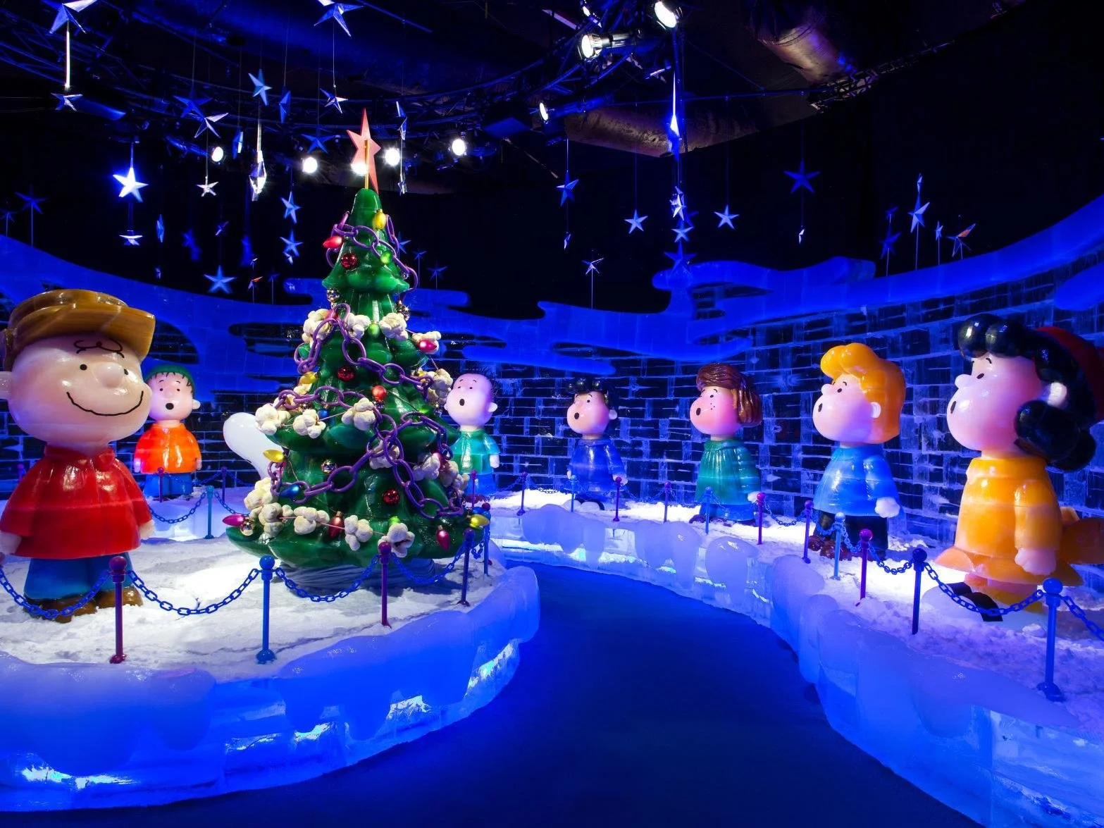 Christmas display featuring large plastic figurines of children around a decorated Christmas tree in an ice-themed setting with blue lighting and star decorations.