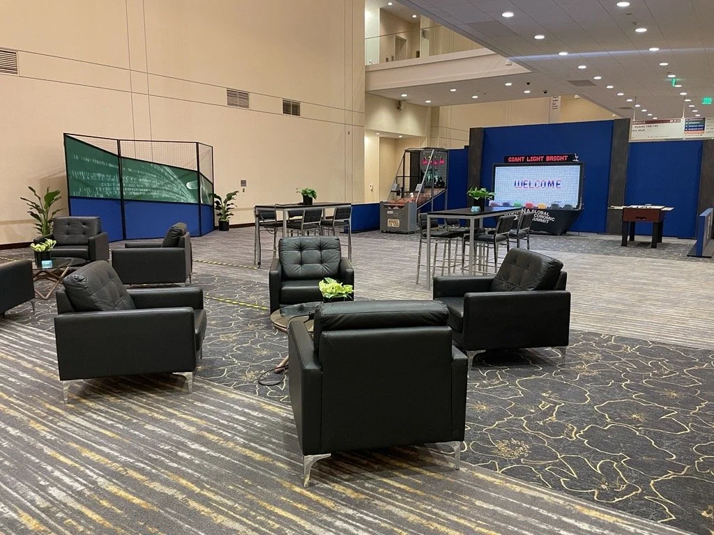 Empty lounge area with black leather chairs, small tables, and a large digital sign in the background at an airport or convention center.
