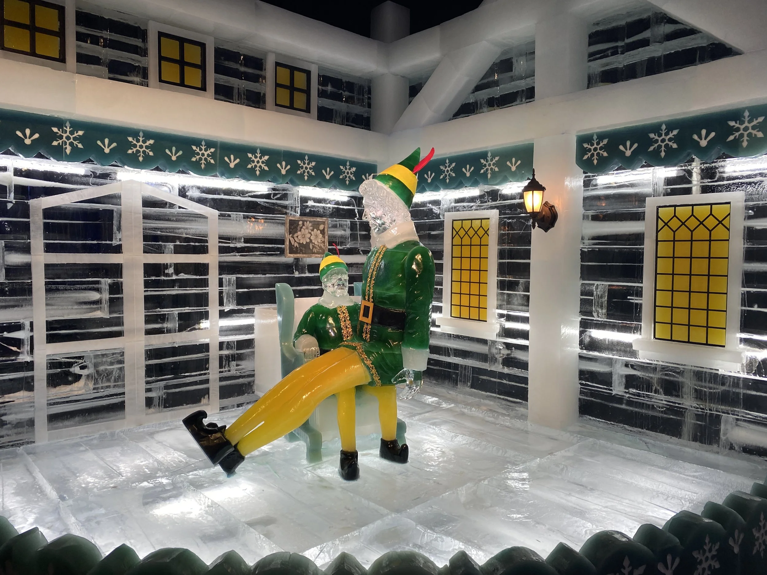 Ice sculpture of Santa Claus and a reindeer with colorful hats inside an ice bar decorated for Christmas.