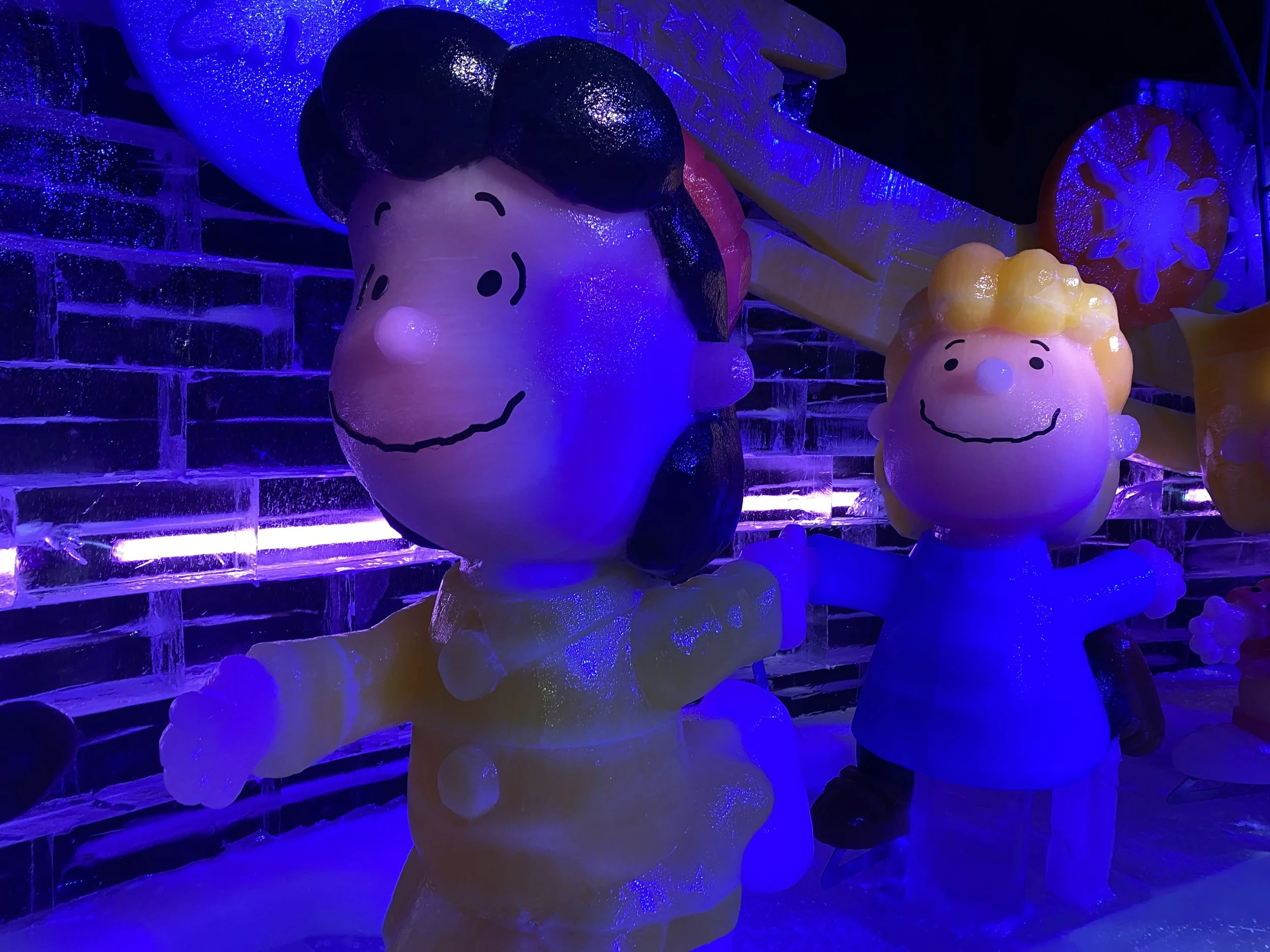 Ice sculpture display featuring characters from Peanuts, including Charlie Brown and Sally, illuminated with blue and purple lights.