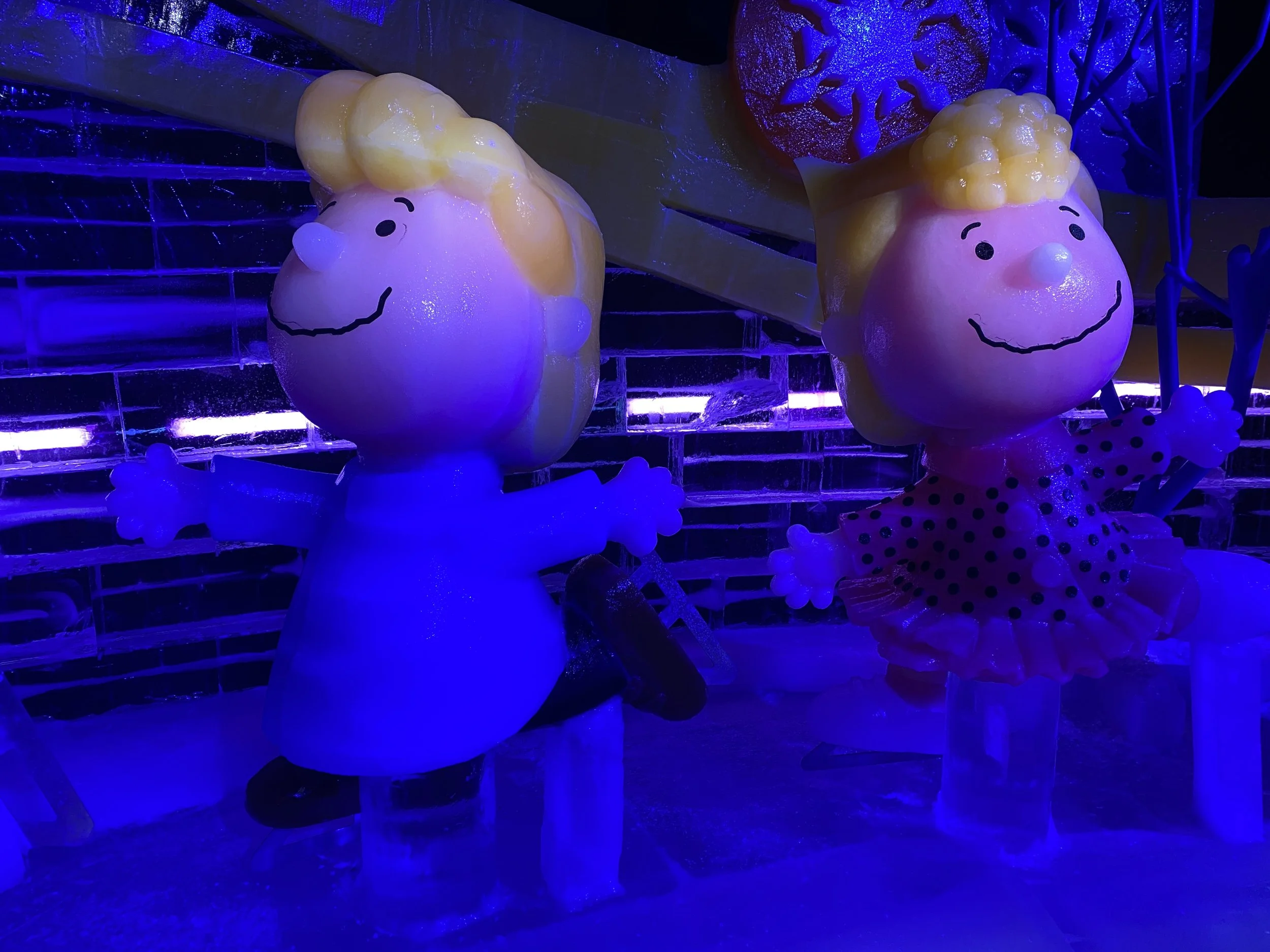 Decorative snowman figures with smiling faces and yellow hats, illuminated by colorful lights in a festive setting.