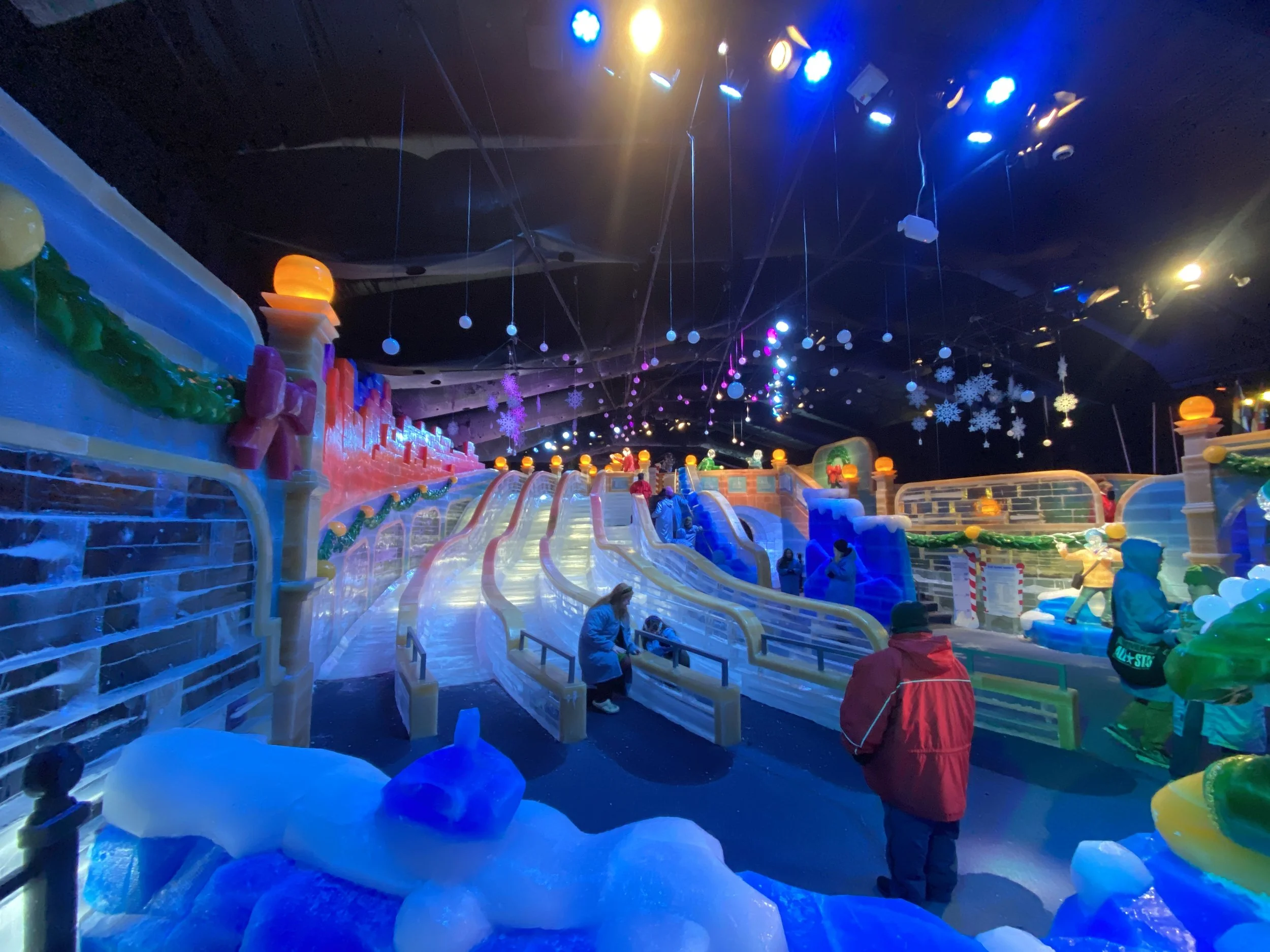 Ice skating rink decorated with holiday-themed snowflakes and ornaments, with children and adults skating and playing.