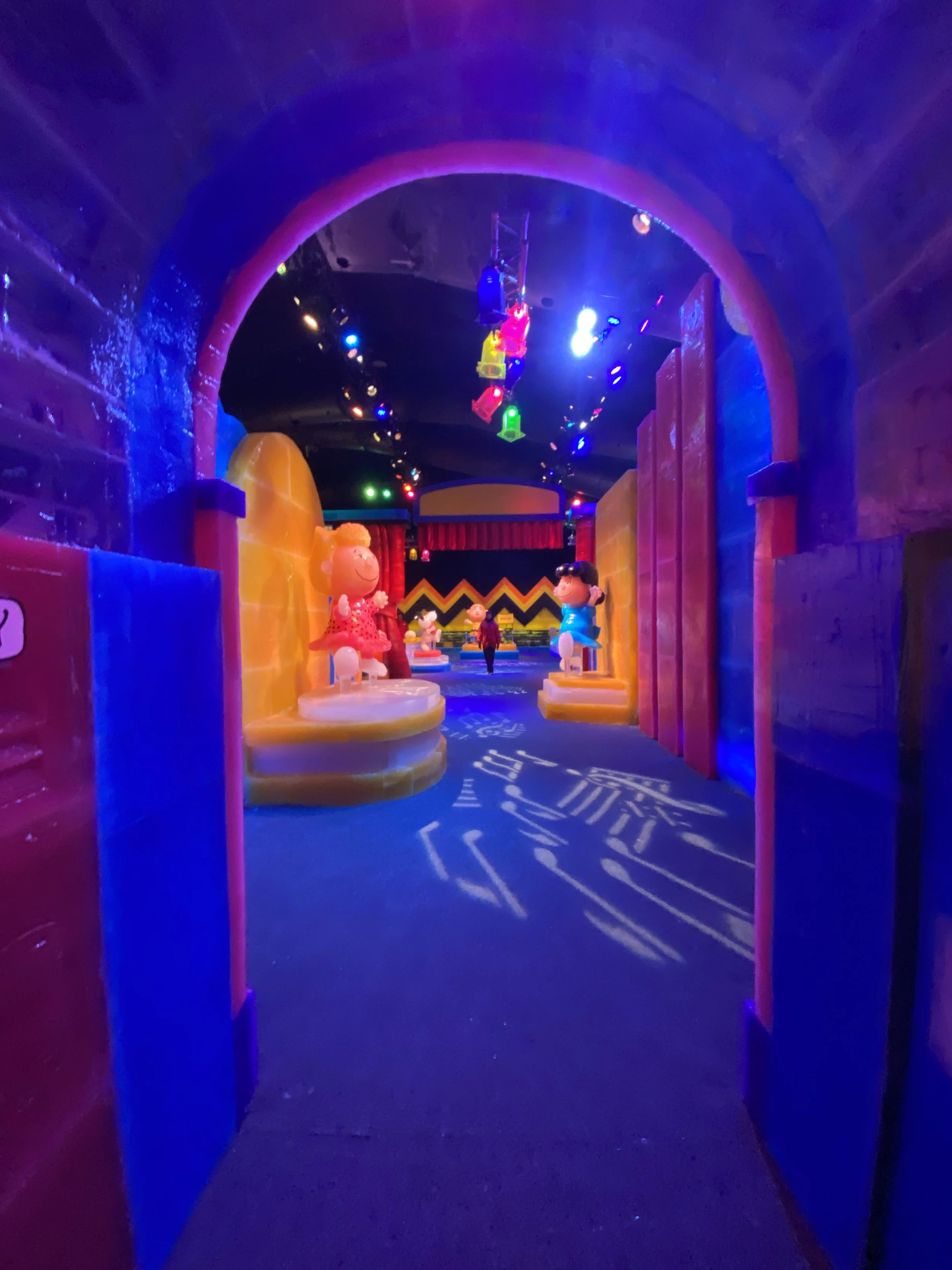 Colorful indoor play area with character statues, arches, and illuminated hanging toys under a dark ceiling.