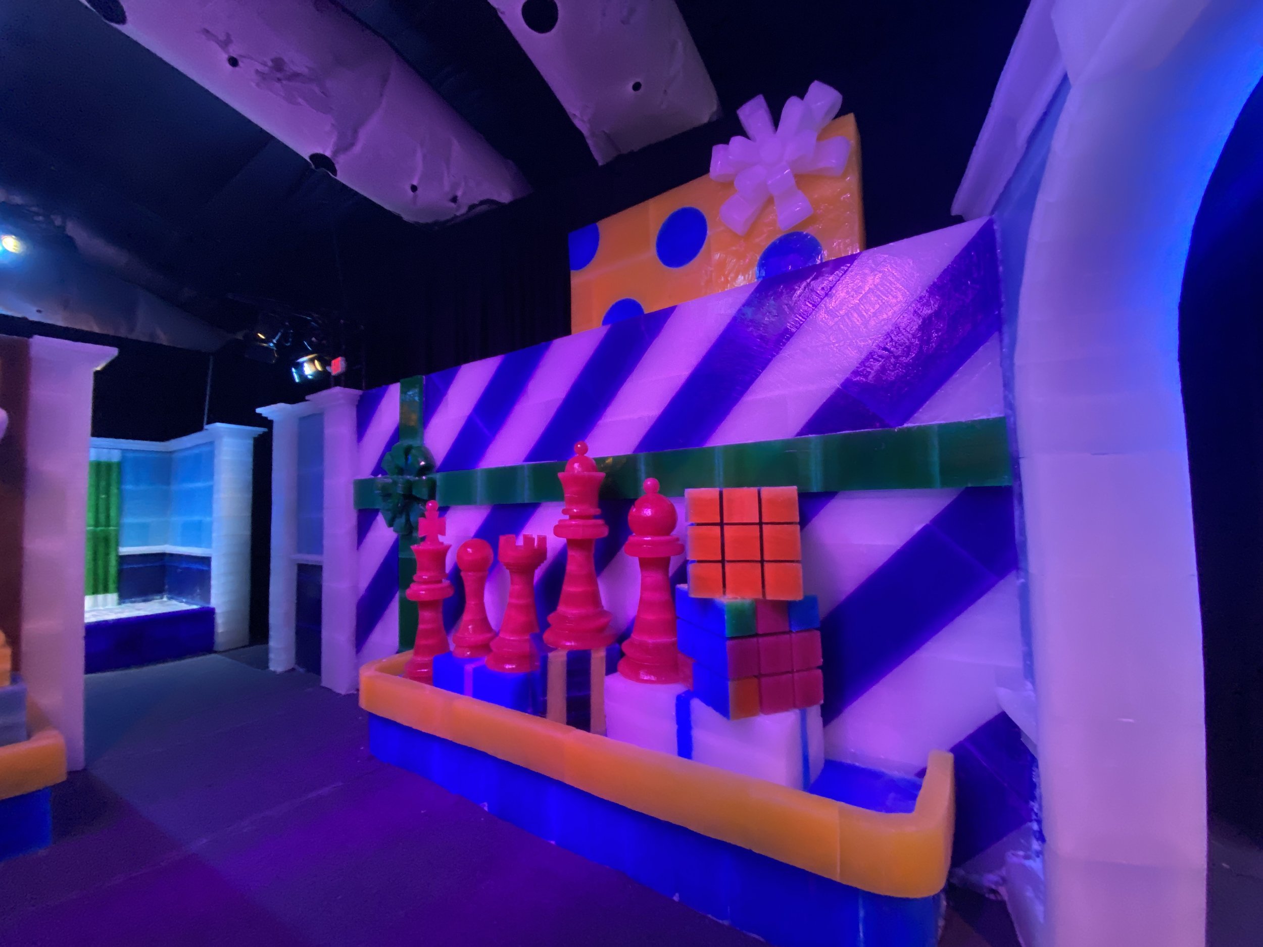 Colorful indoor climbing wall with artificial blocks and holds, illuminated by blue and purple lights.