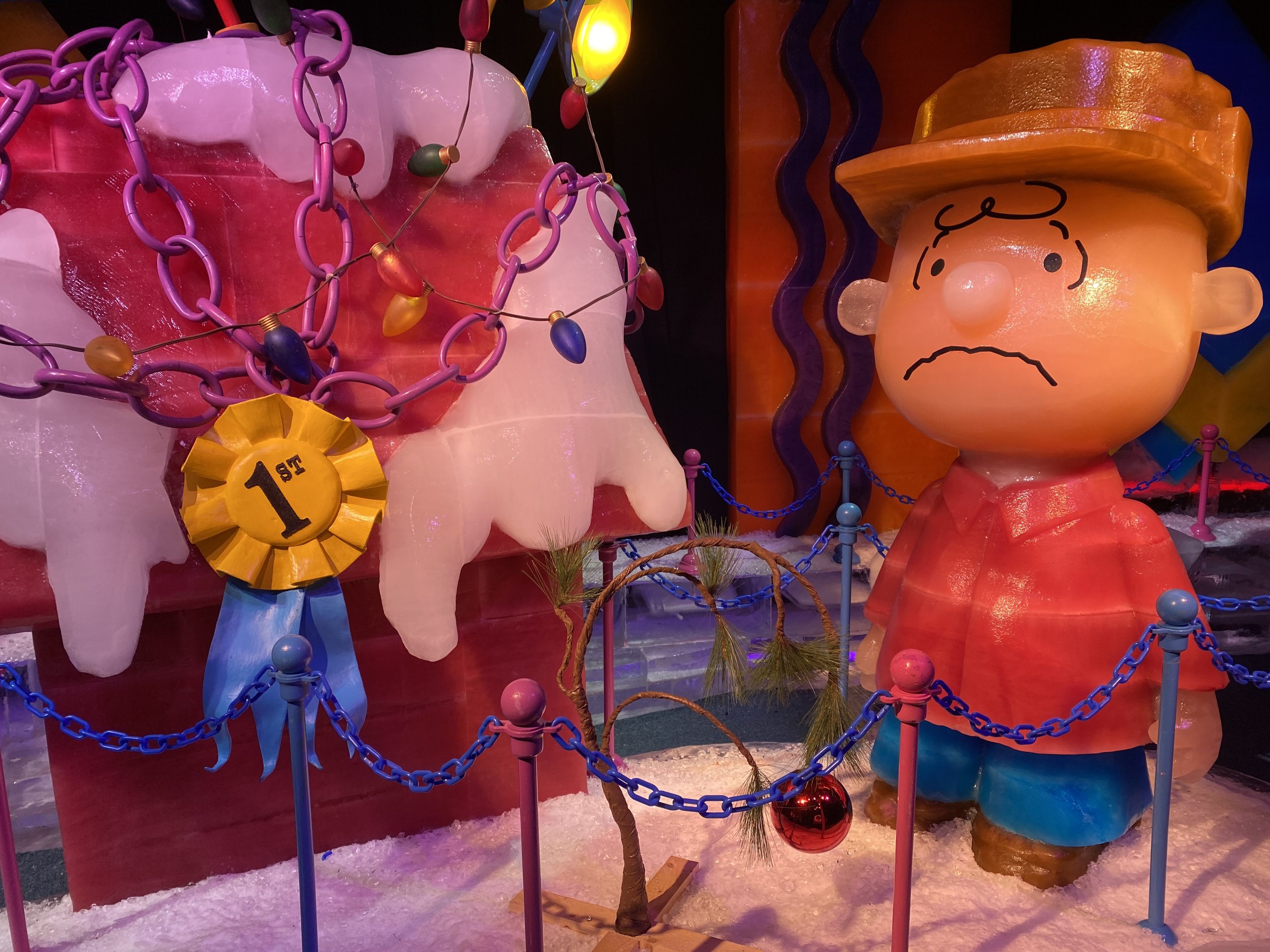 Colorful display of cartoon-like sculptures, including a large hamburger with a face wearing a bun hat, a pink ice cream cone with a yellow ribbon marked '1st,' and various decorative chains and lights.