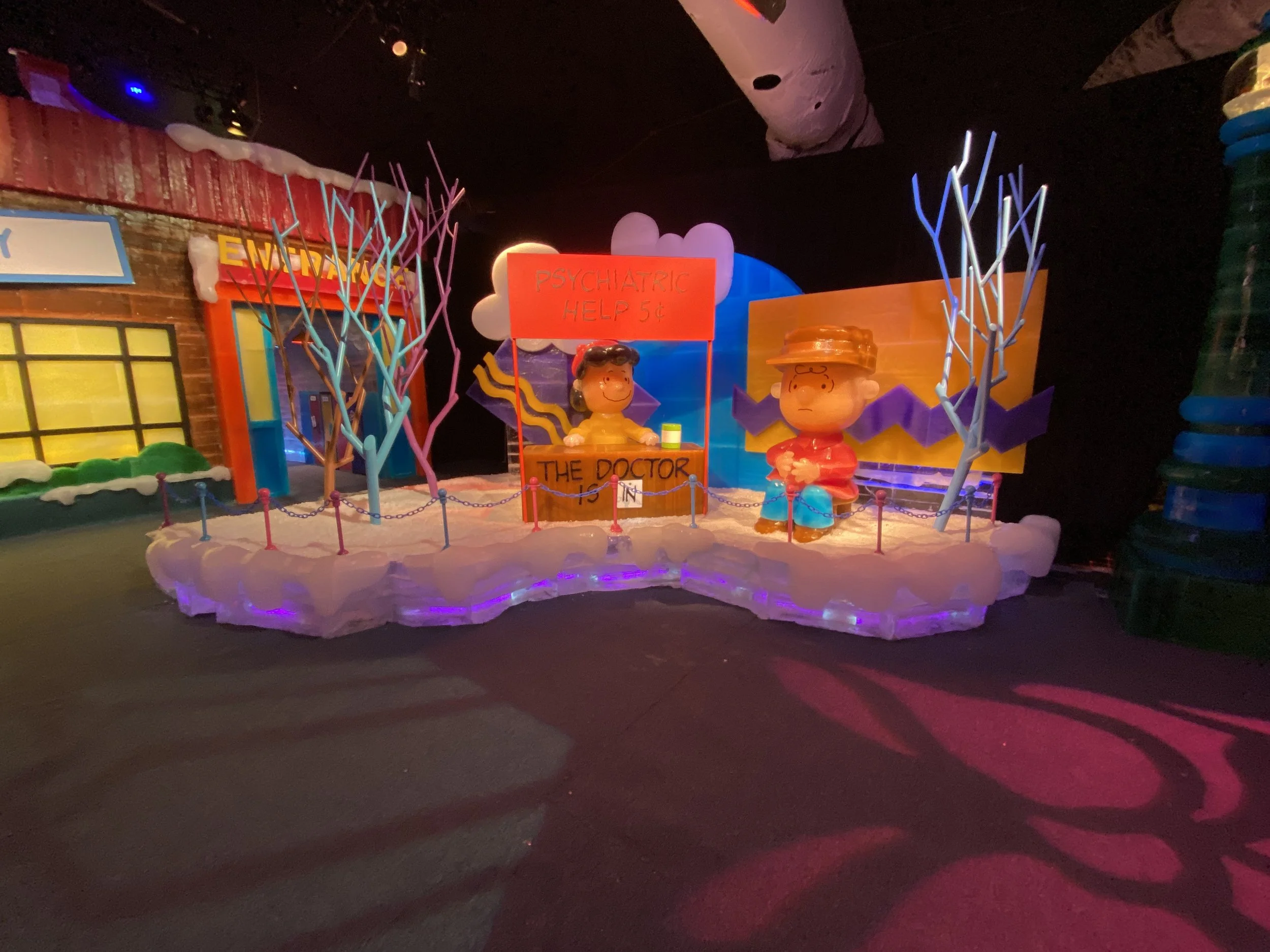 Colorful indoor scene featuring cartoon character statues, a sign for psychiatric help costing 5 cents, and whimsical decorations with lighting.