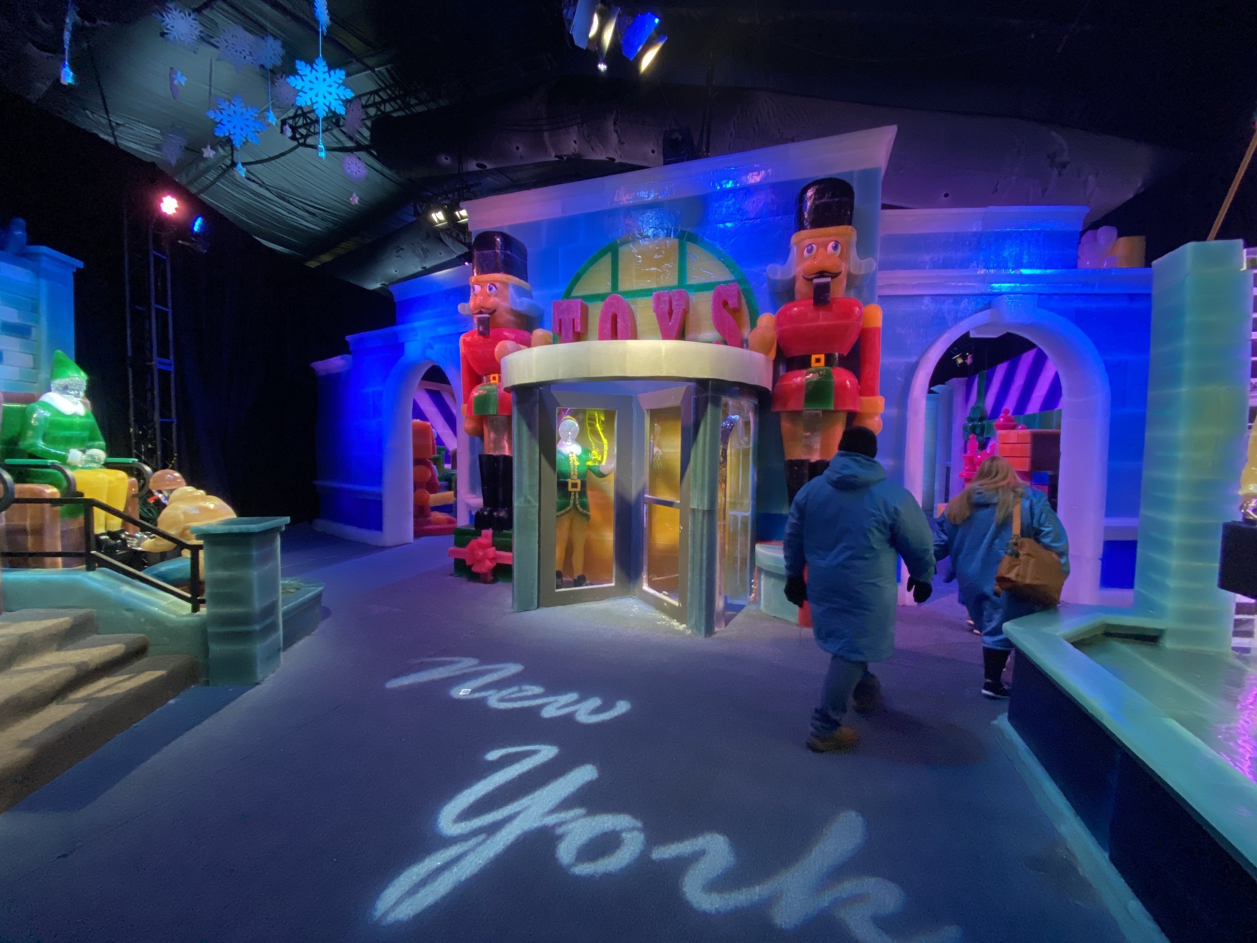 Indoor holiday display featuring large illuminated nutcracker figures, snowflake decorations hanging from the ceiling, and a colorful castle-like structure with festive lighting.