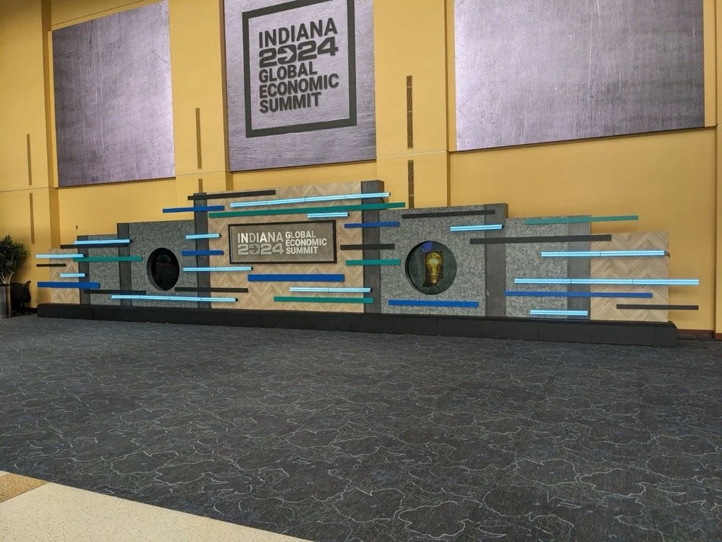 Decorative wall display at Indiana 2024 Global Economic Summit, with colored horizontal light bars and a logo of a lightbulb.