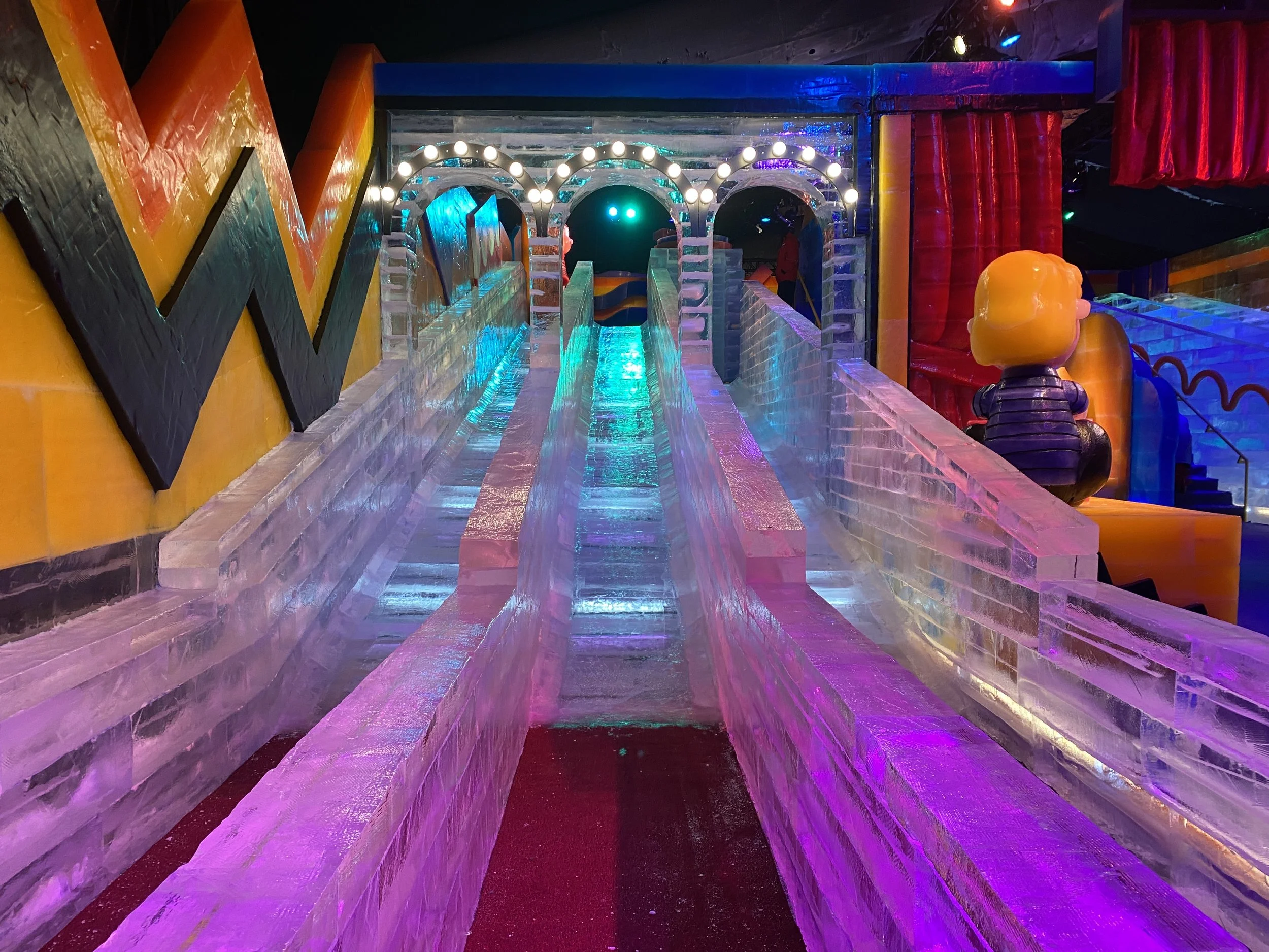 Ice slide with rainbow lighting and colorful decor at an indoor ice attraction.