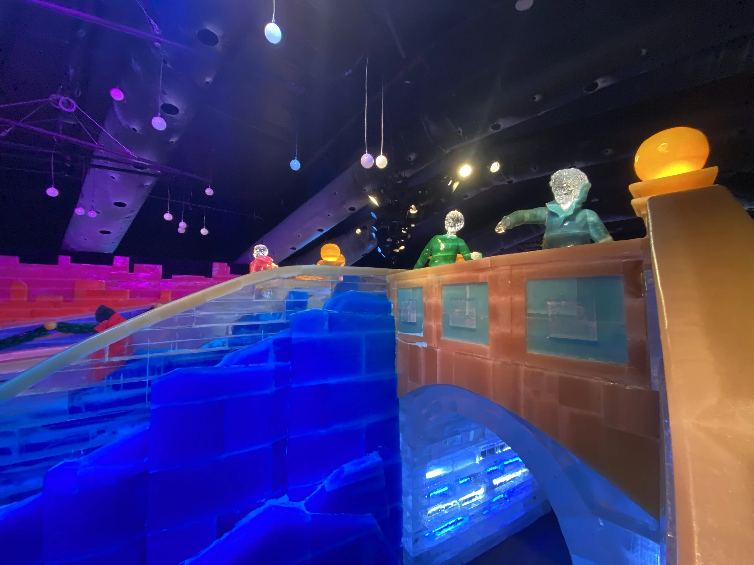 Colorful indoor scene with illuminated figures, hanging lights, and vibrant decorations.